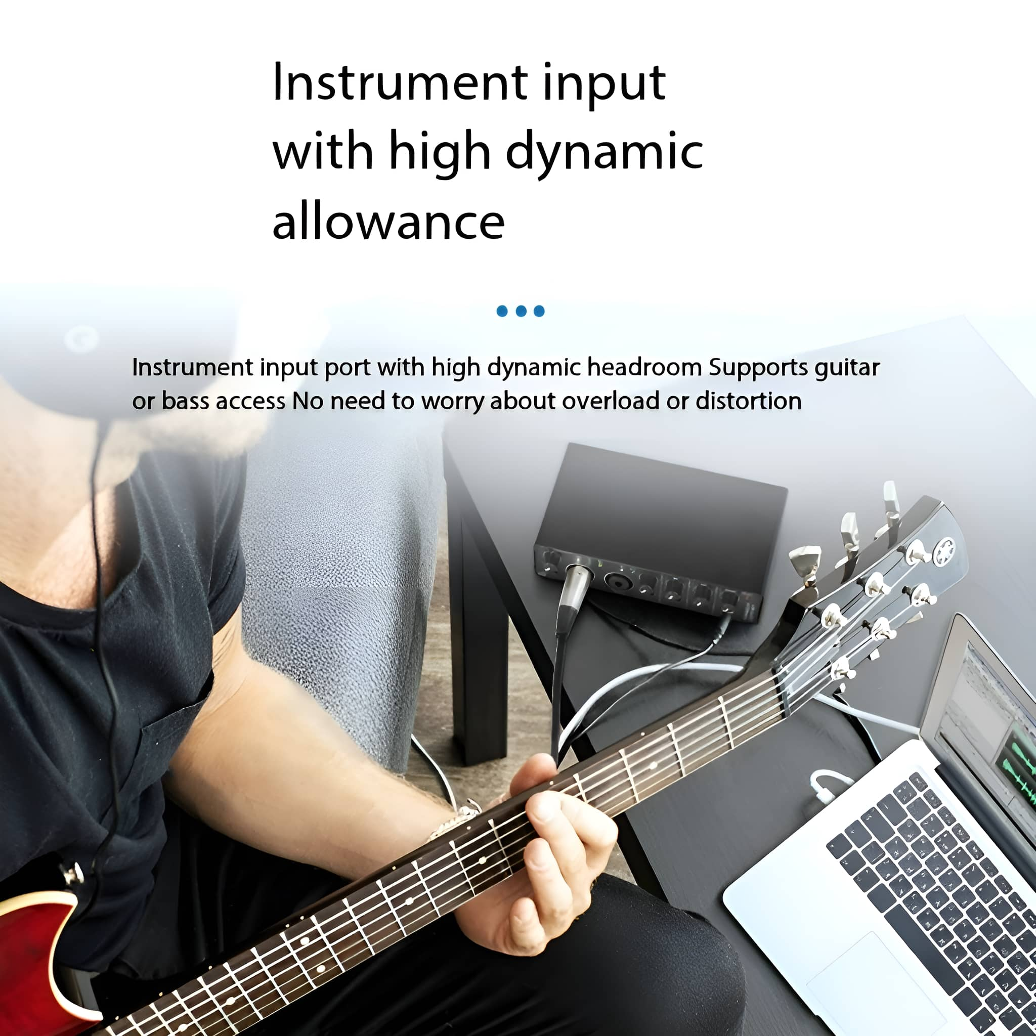 Eine Person spielt Gitarre. Ein Laptop und Audio-Interface sind auf einem Tisch.