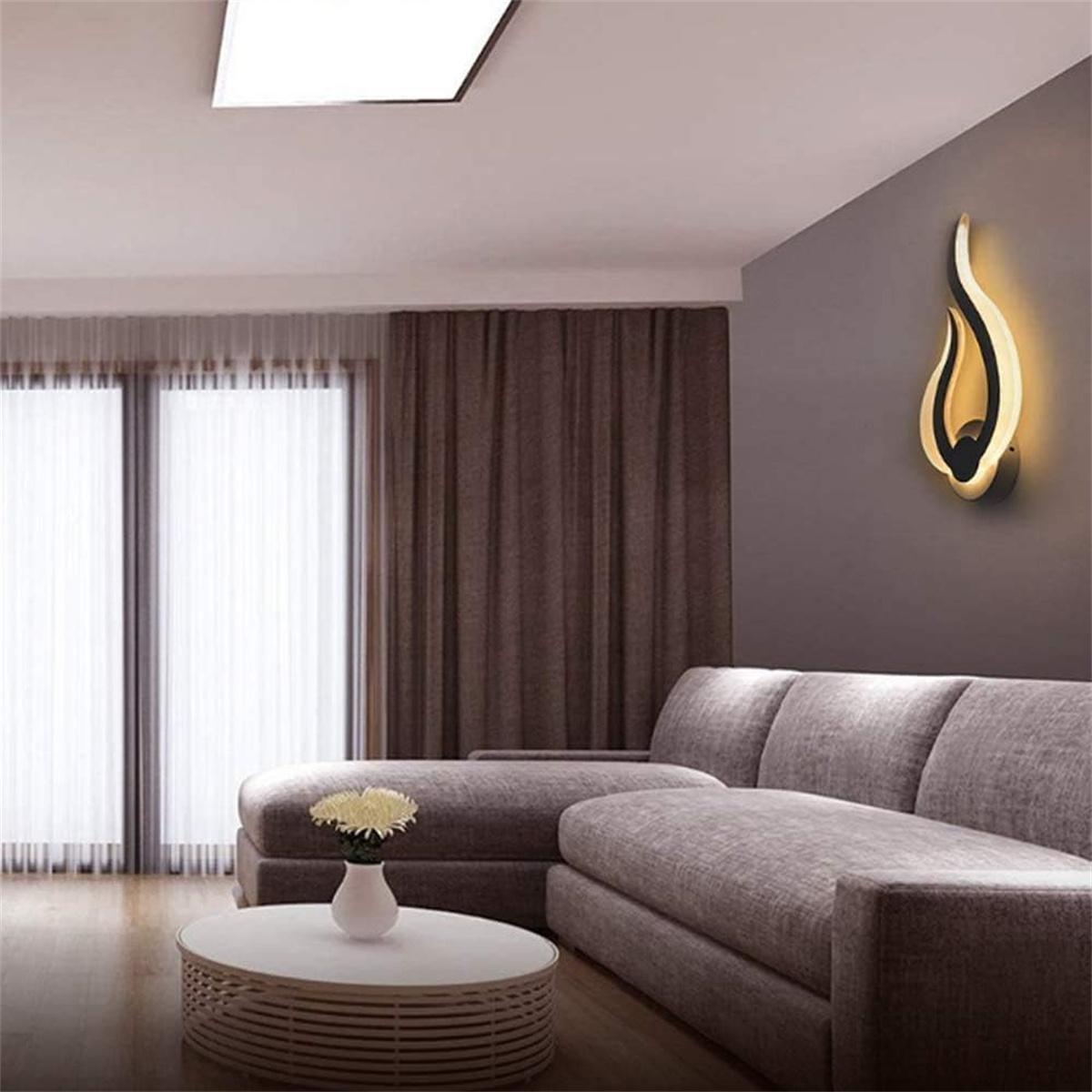 Ein modernes Wohnzimmer mit einer Wandleuchte und einem Sofa. Tisch mit Vase und Blumen.