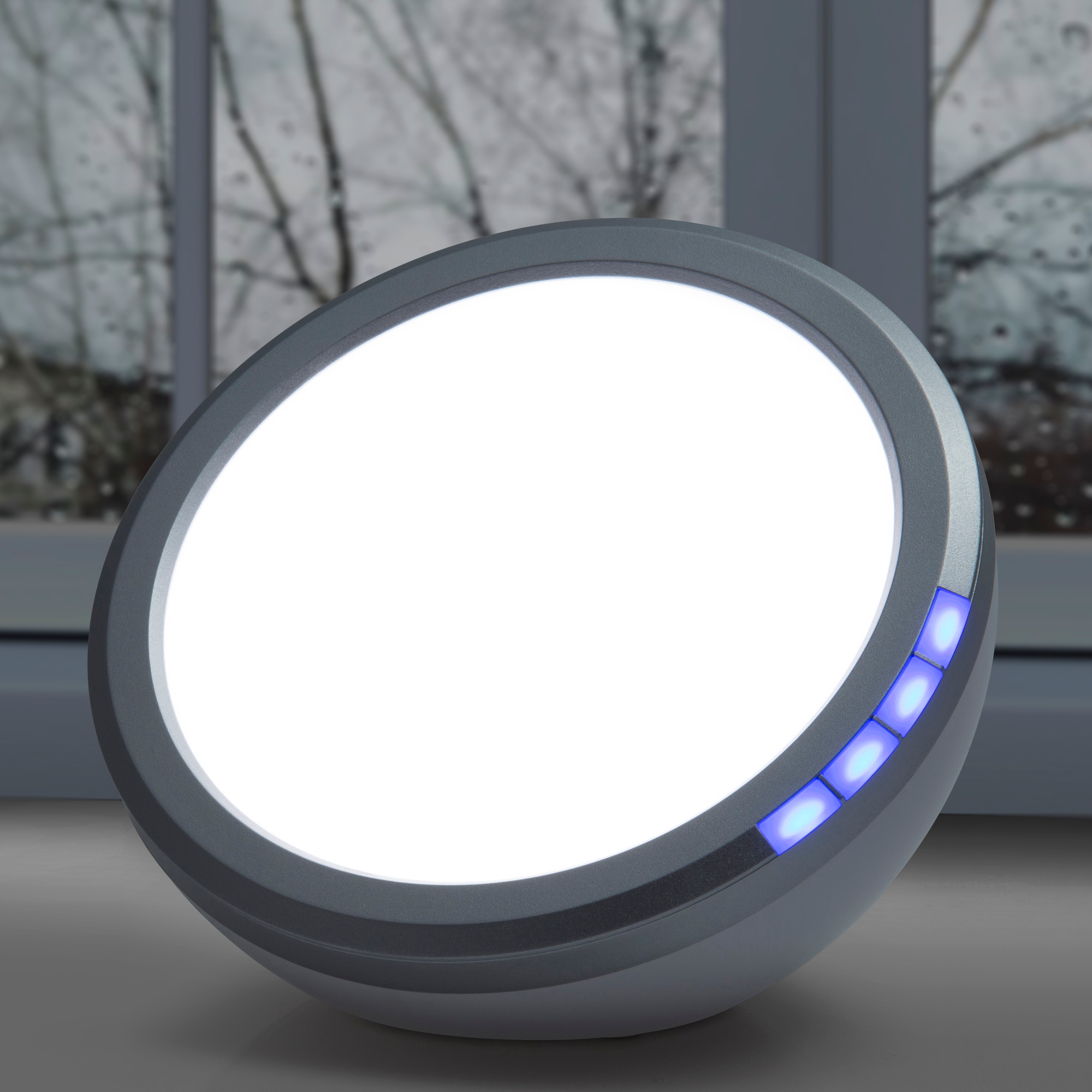 Eine weiße, kreisförmige SAD-Lampe mit blauen Lichtern. Sie steht auf einer Holzoberfläche in Fensternähe.
