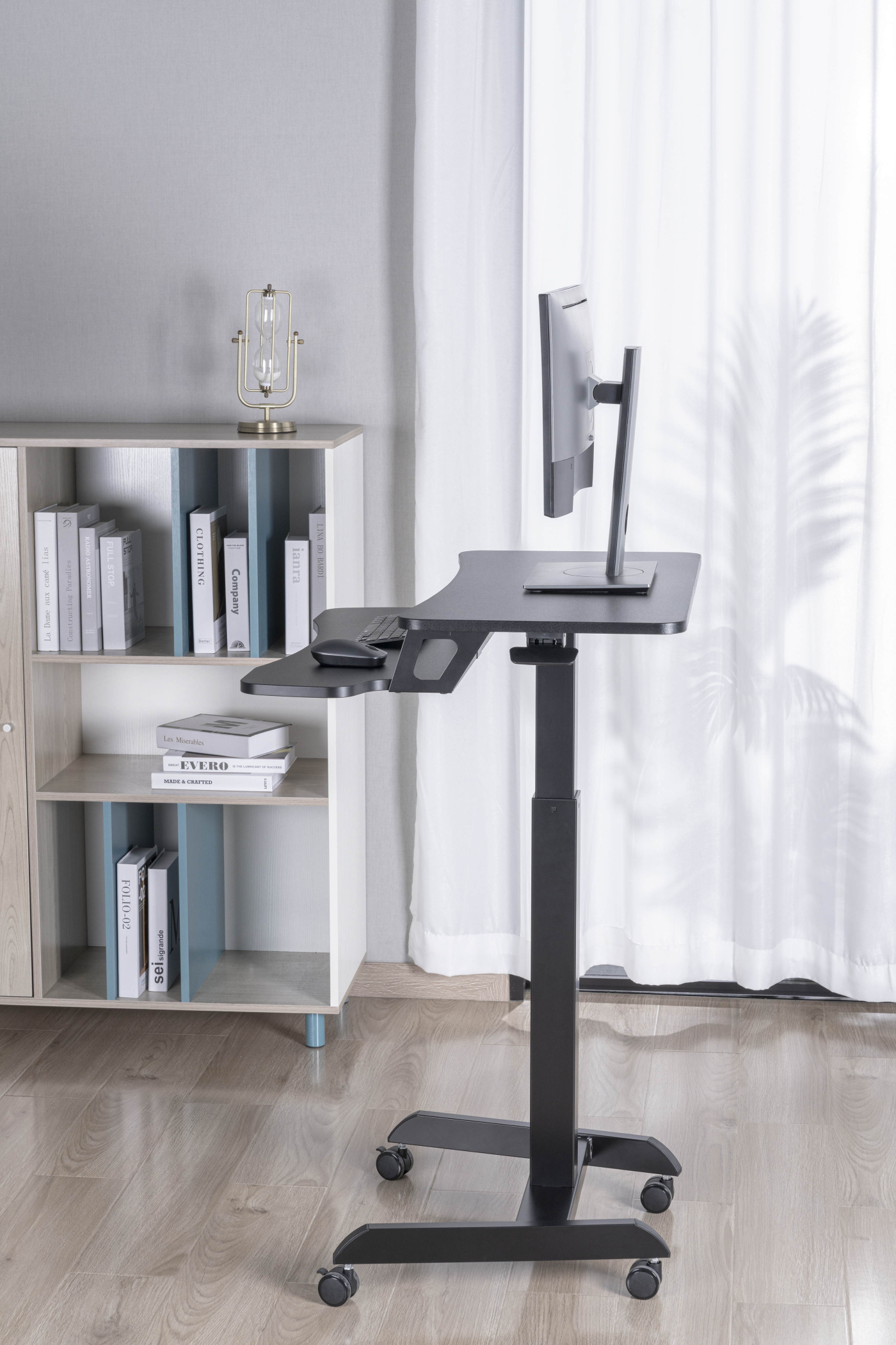 Zwart staand bureau met een monitor en een toetsenbord. Een boekenplank links.