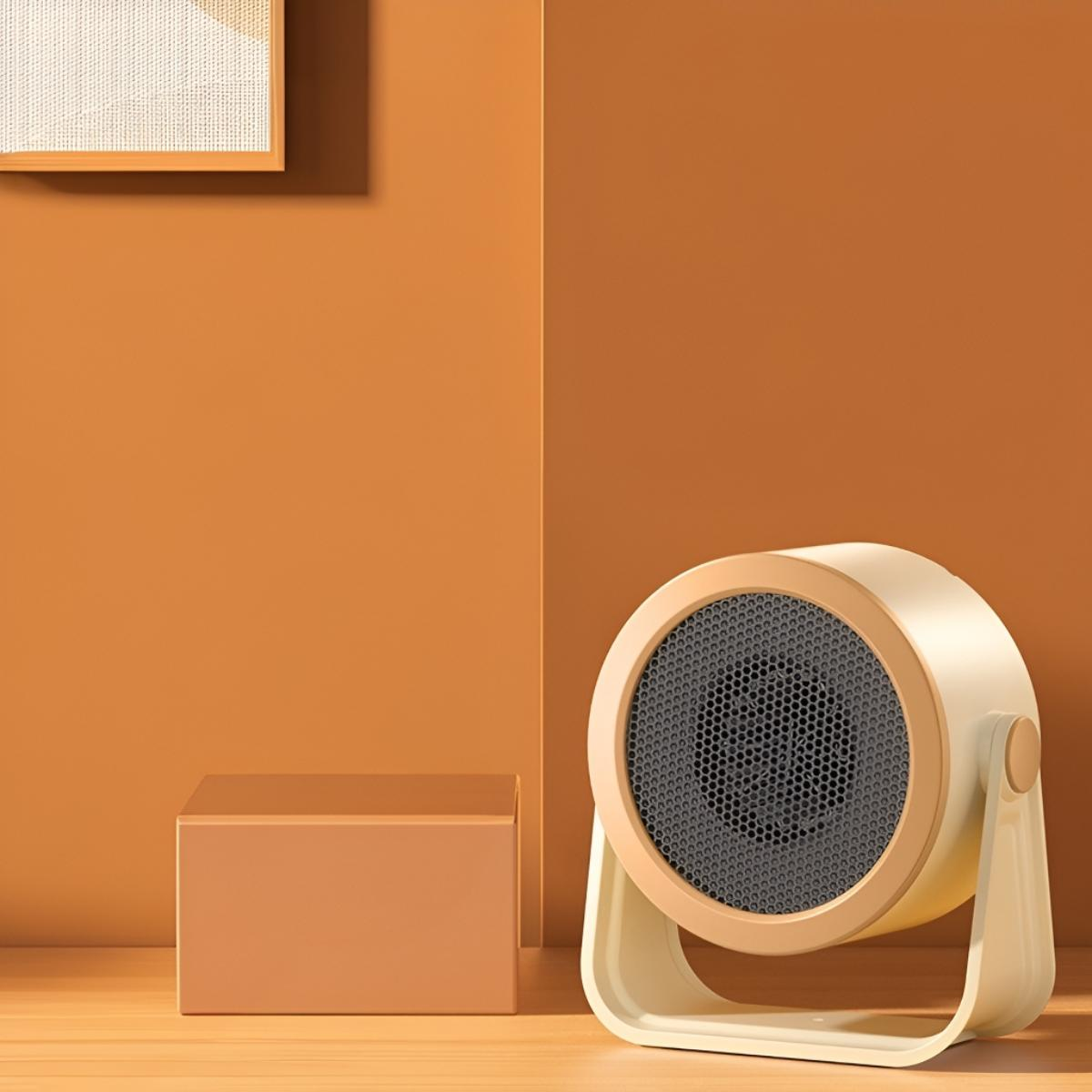 Kleiner beige-brauner Heizlüfter auf einer Holzoberfläche. Hintergrund ist orange und ein kleiner Würfel.