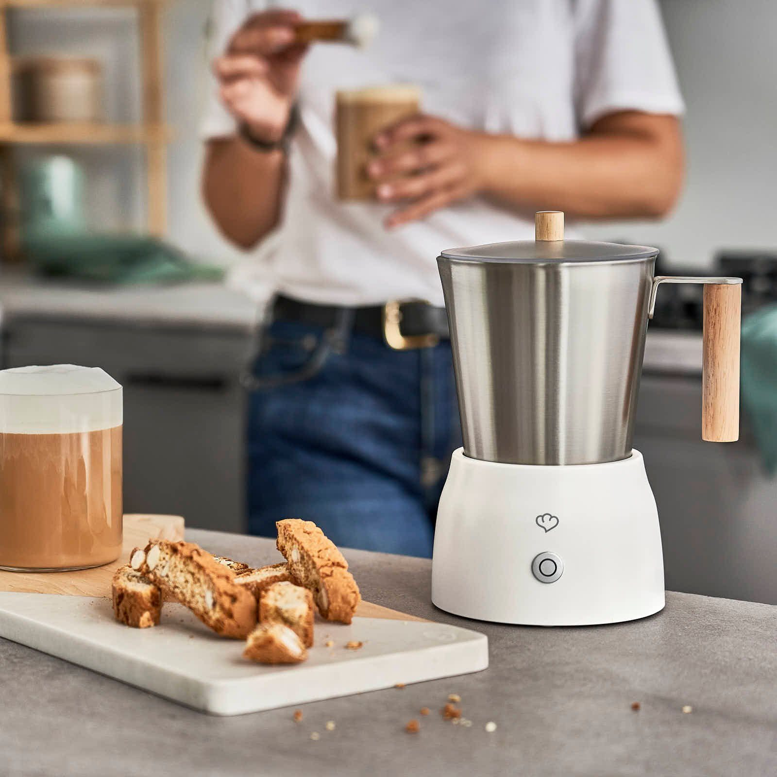 Ein Milchaufschäumer mit einer Person, die ein Getränk zubereitet. Es gibt Biscotti und ein Glas Kaffee.