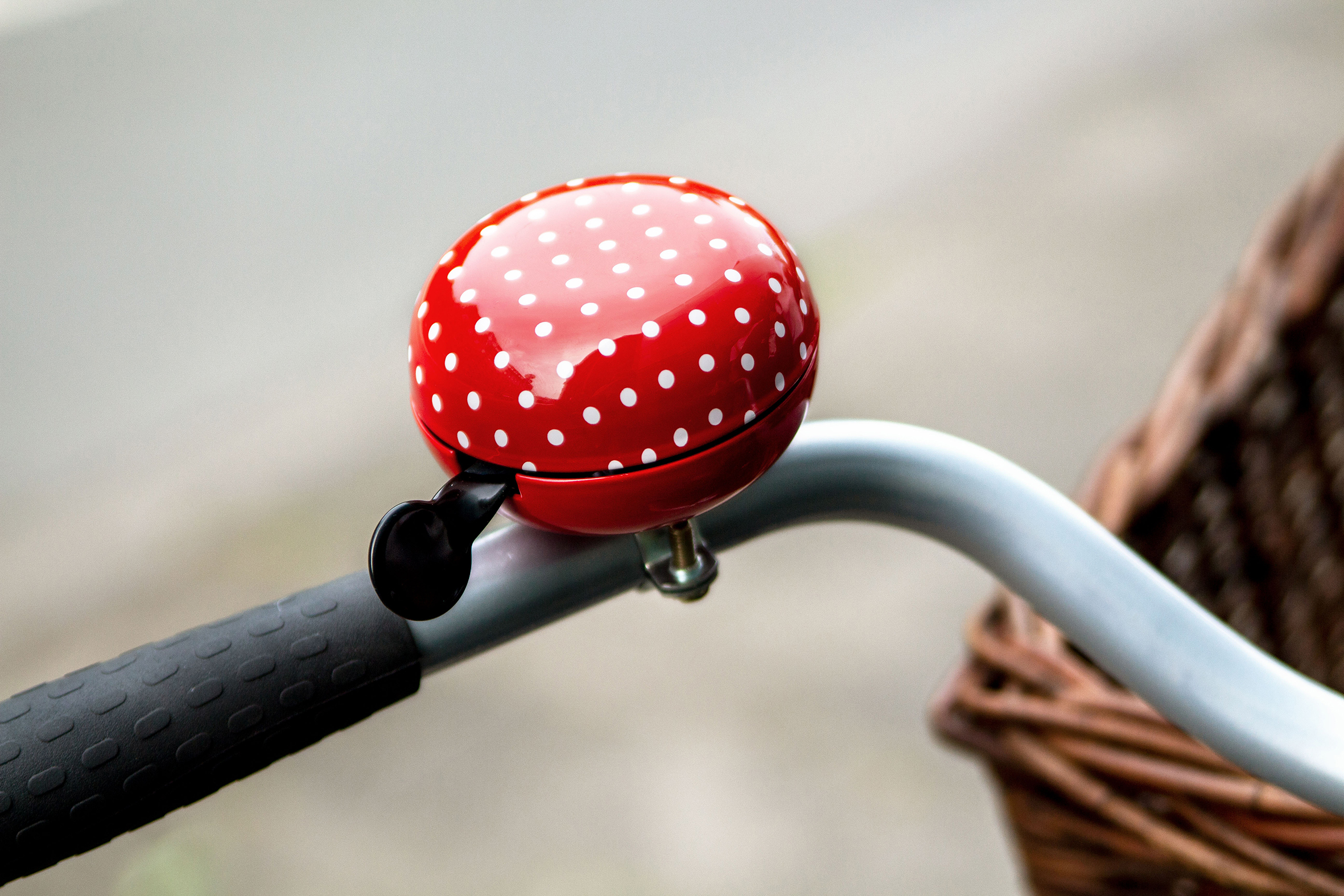 Eine rote Fahrradklingel mit weißen Punkten, an einem Lenker neben einem Korb montiert.