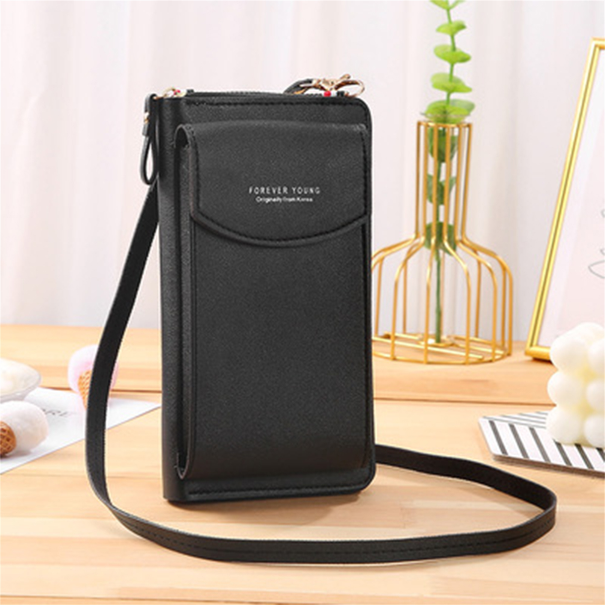 Eine schwarze, lange Telefontasche mit Schulterriemen auf weißem Hintergrund. Sie sagt 'Forever Young'.