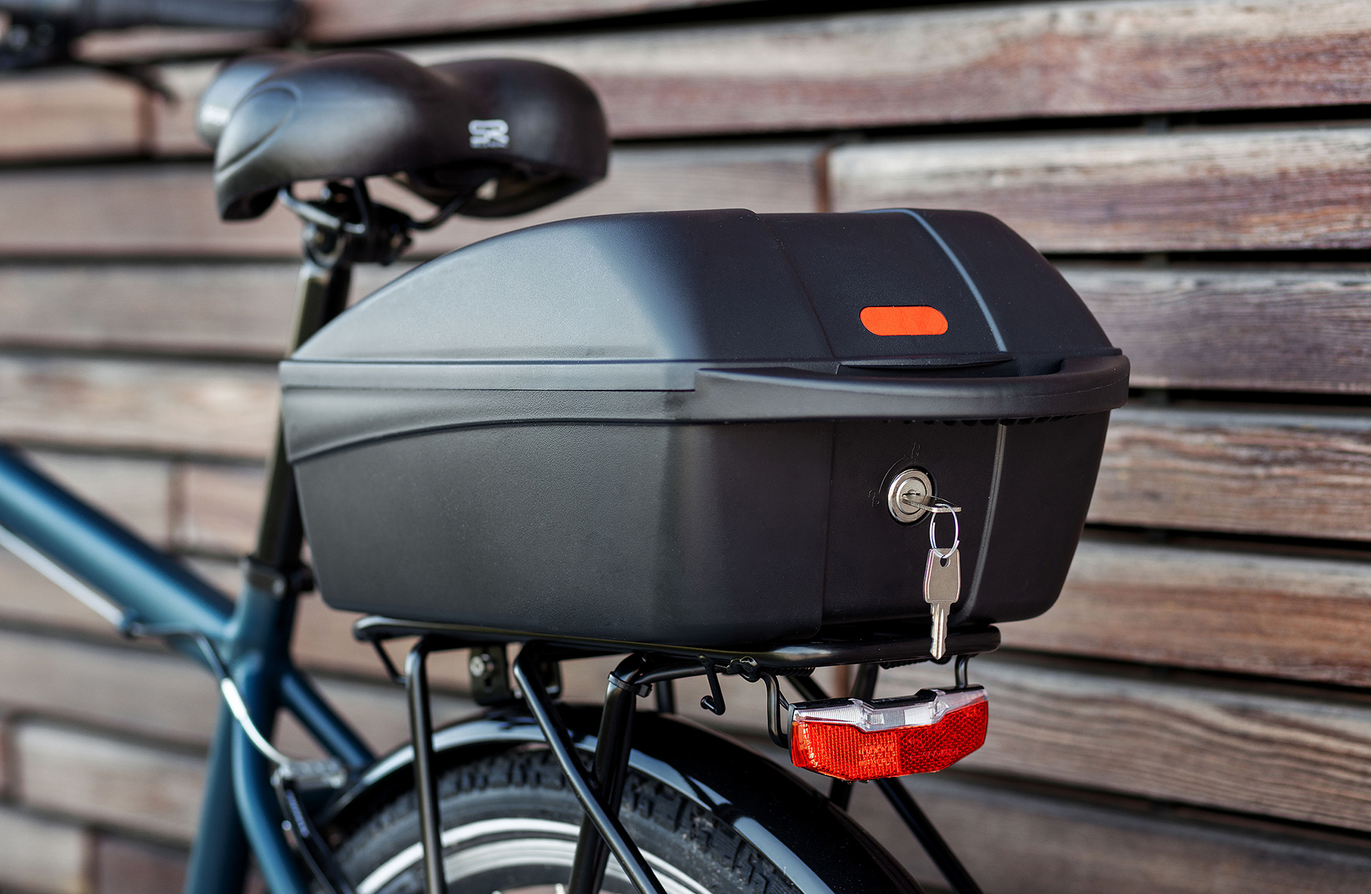 Eine schwarze Fahrrad-Cargo-Box an einem Fahrrad montiert. Die Box hat einen Schlüssel im Schloss und einen roten Reflektor.