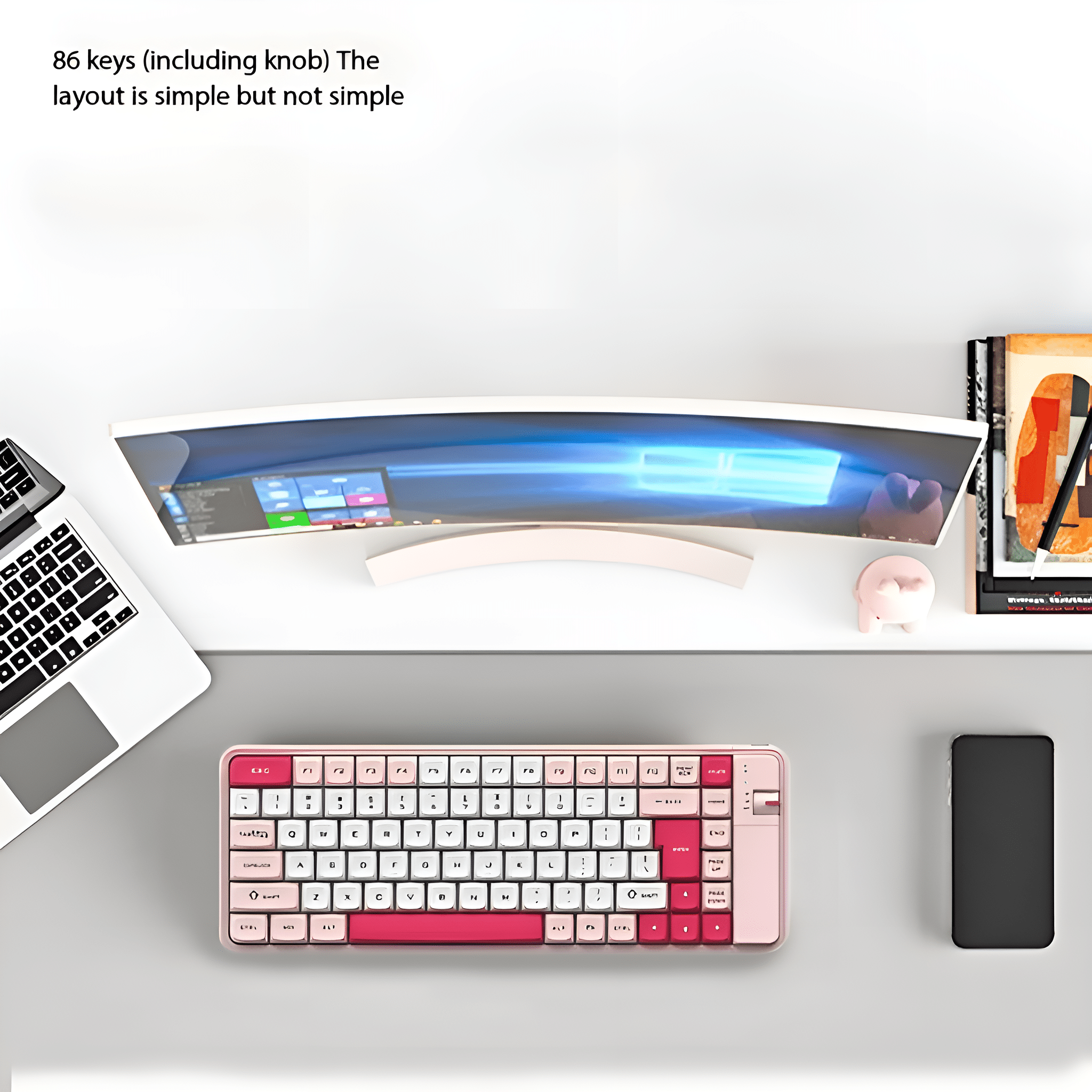 Eine rosa-weiße Tastatur liegt auf einem Schreibtisch mit Monitor, Laptop, Büchern und Telefon.