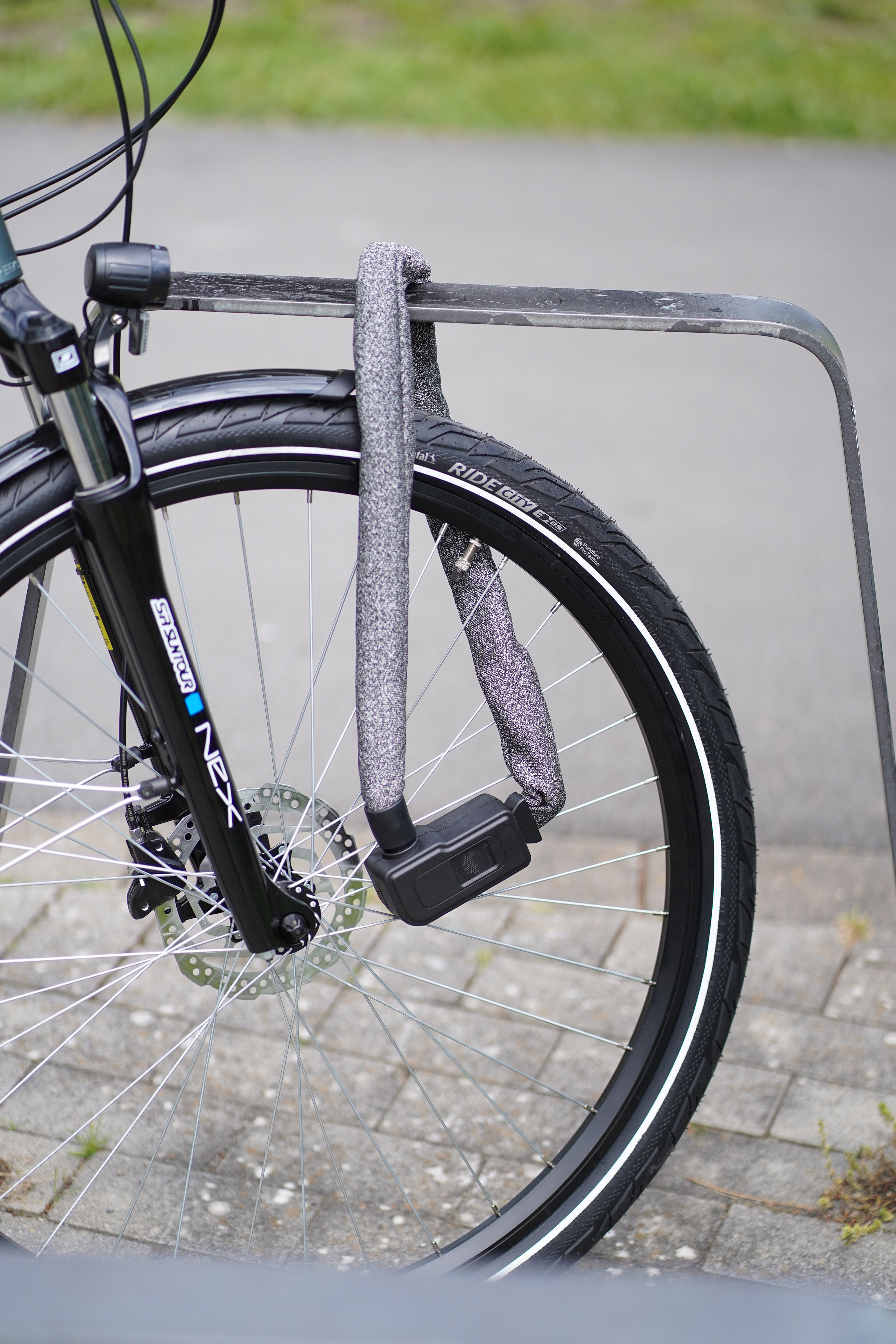 Ein Fahrradrad, das mit einem Kettenschloss an einem Fahrradständer aus Metall befestigt ist.