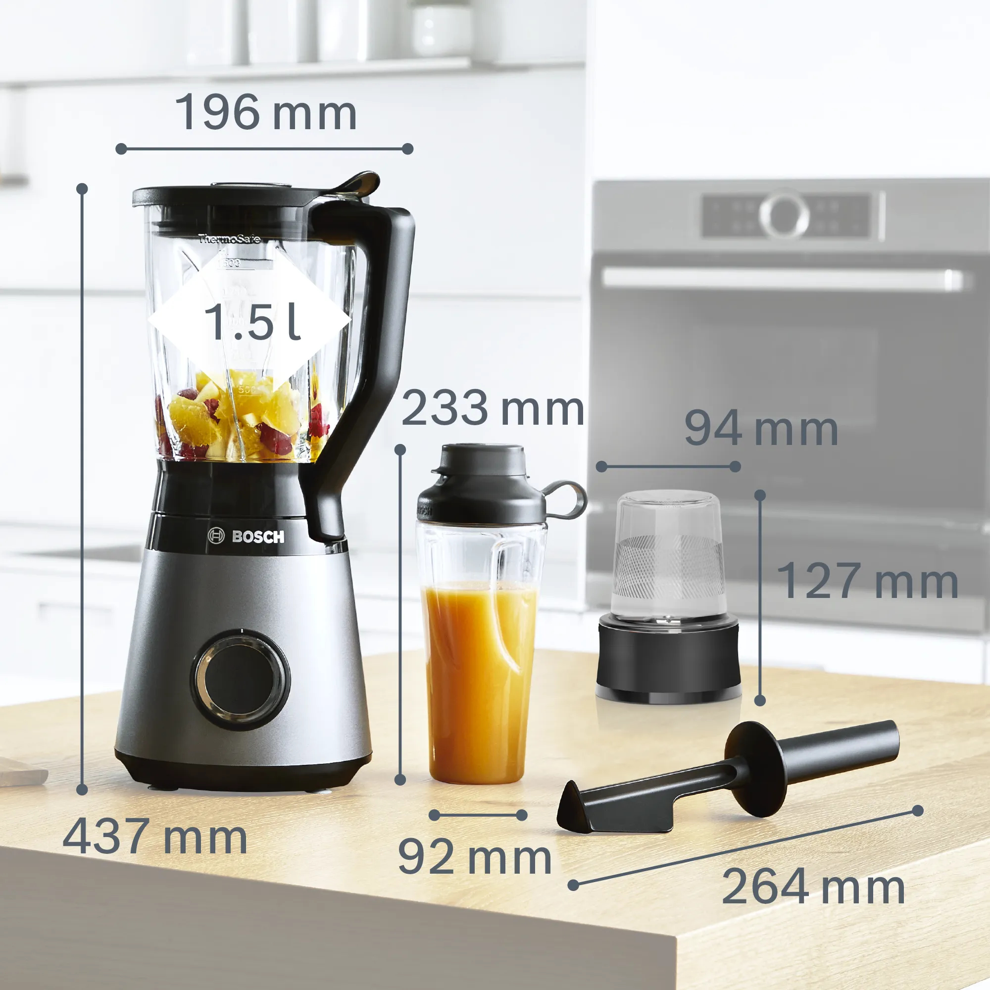 Frullatore con frutta all'interno, uno shaker e altri accessori, con dimensioni etichettate su un tavolo.