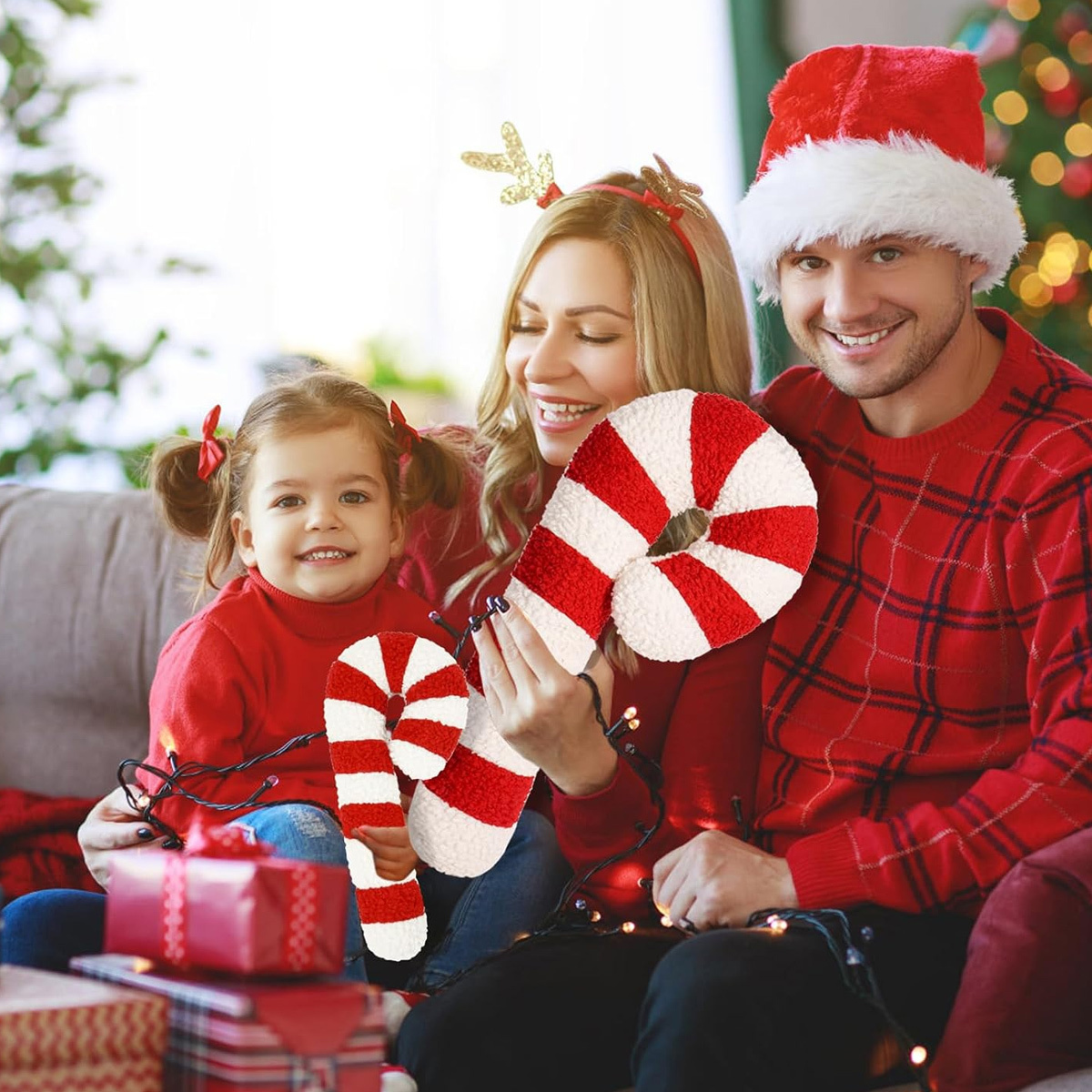 Eine Familie auf einer Couch mit Weihnachtsdekorationen. Sie halten Zuckerstangen und tragen rote Pullover und Hüte.