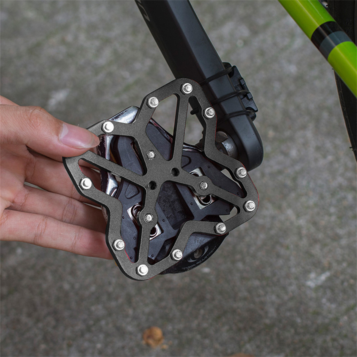 Eine Hand, die ein Fahrradpedal hält. Das Pedal ist schwarz und hat mehrere Löcher und einen silbernen Rahmen.