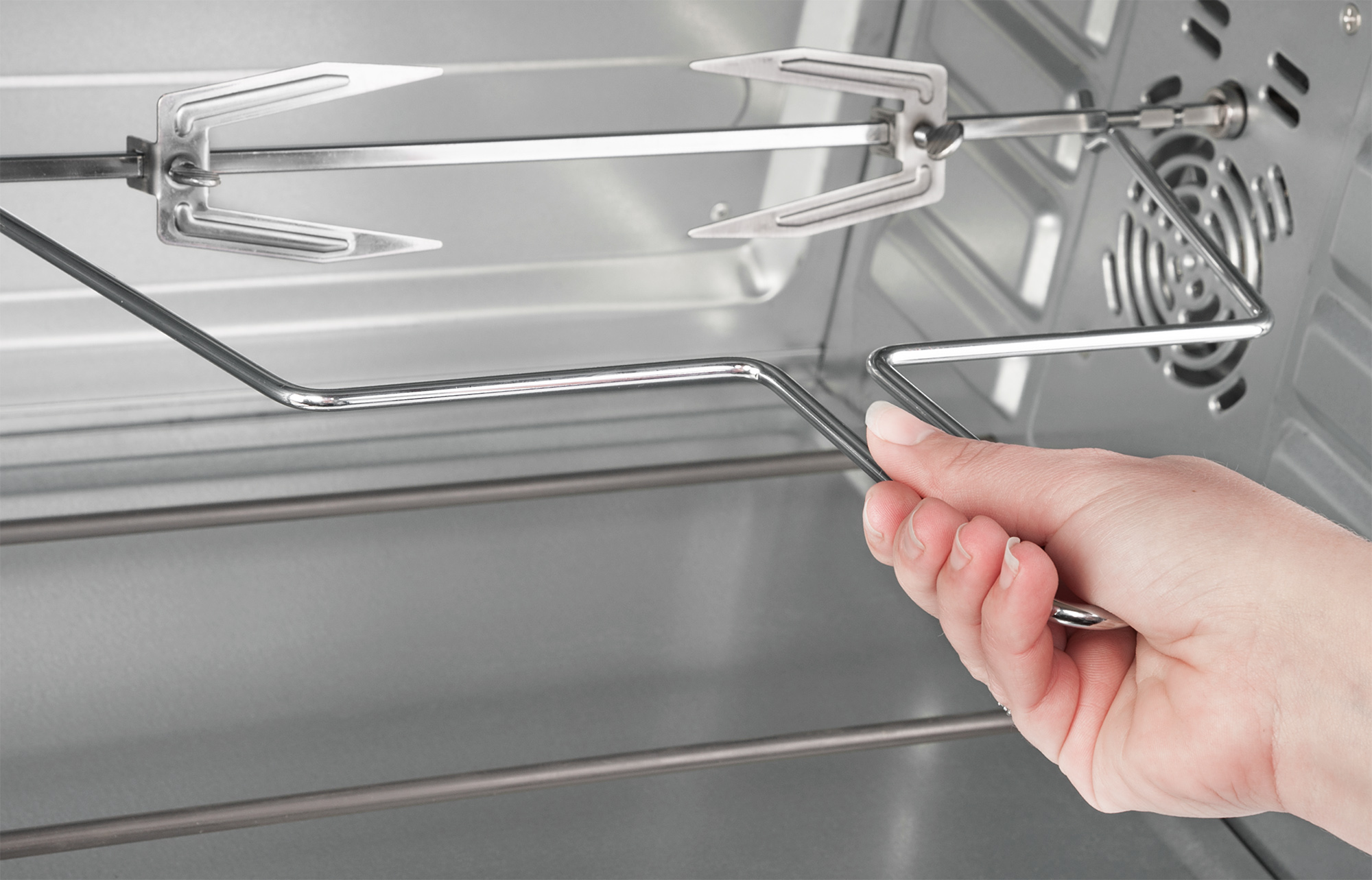 Eine Hand hält einen Metall-Drehspieß in einem Ofen. Der Ofen ist leer und sauber.
