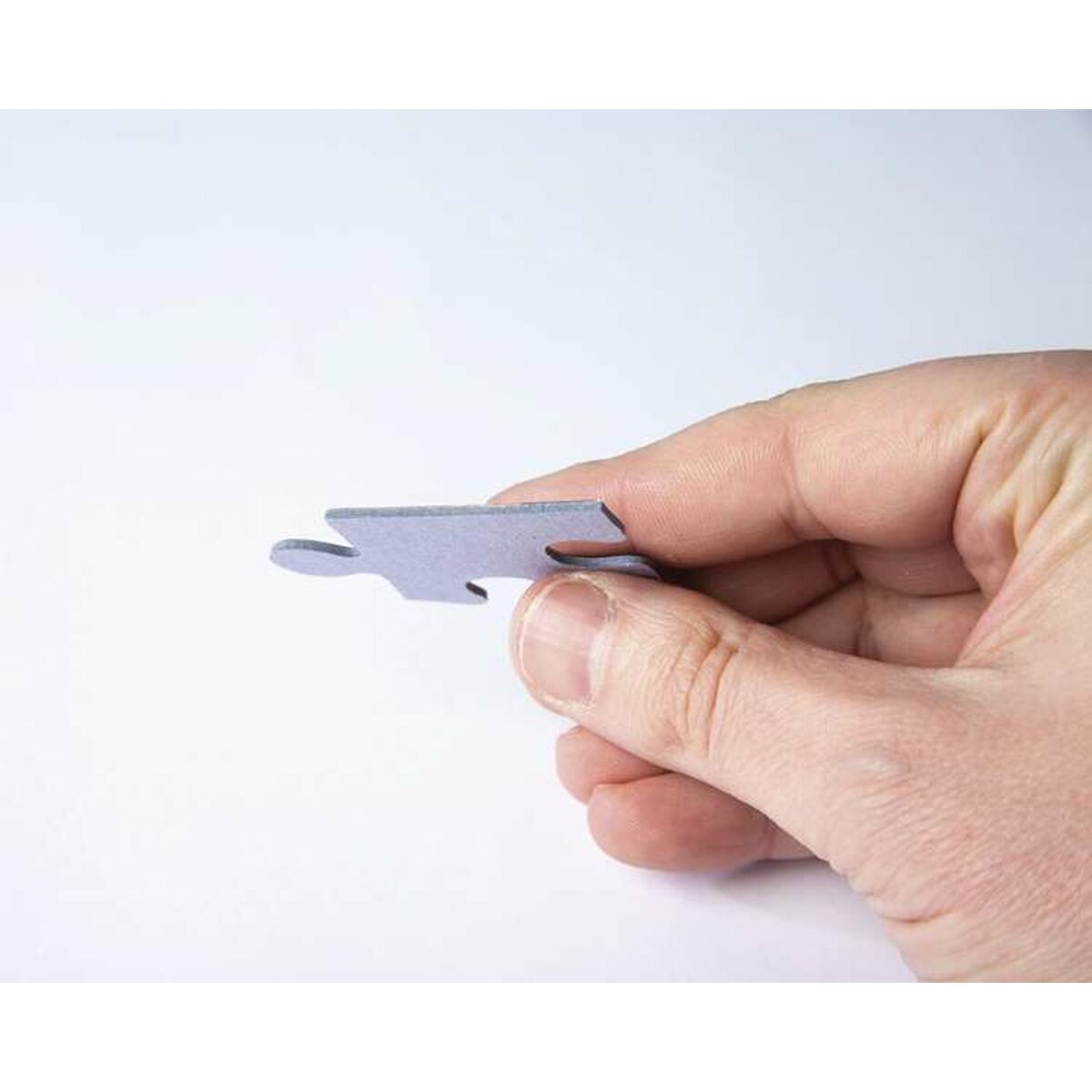 Dłoń trzyma szary element układanki na białym tle. Element ma unikalny kształt, widać palce.