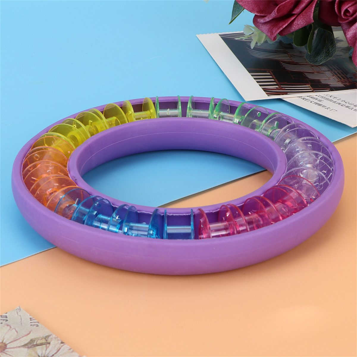 Ein violetter Ring mit bunten Kunststoffspulen. Der Hintergrund ist blau und orange.