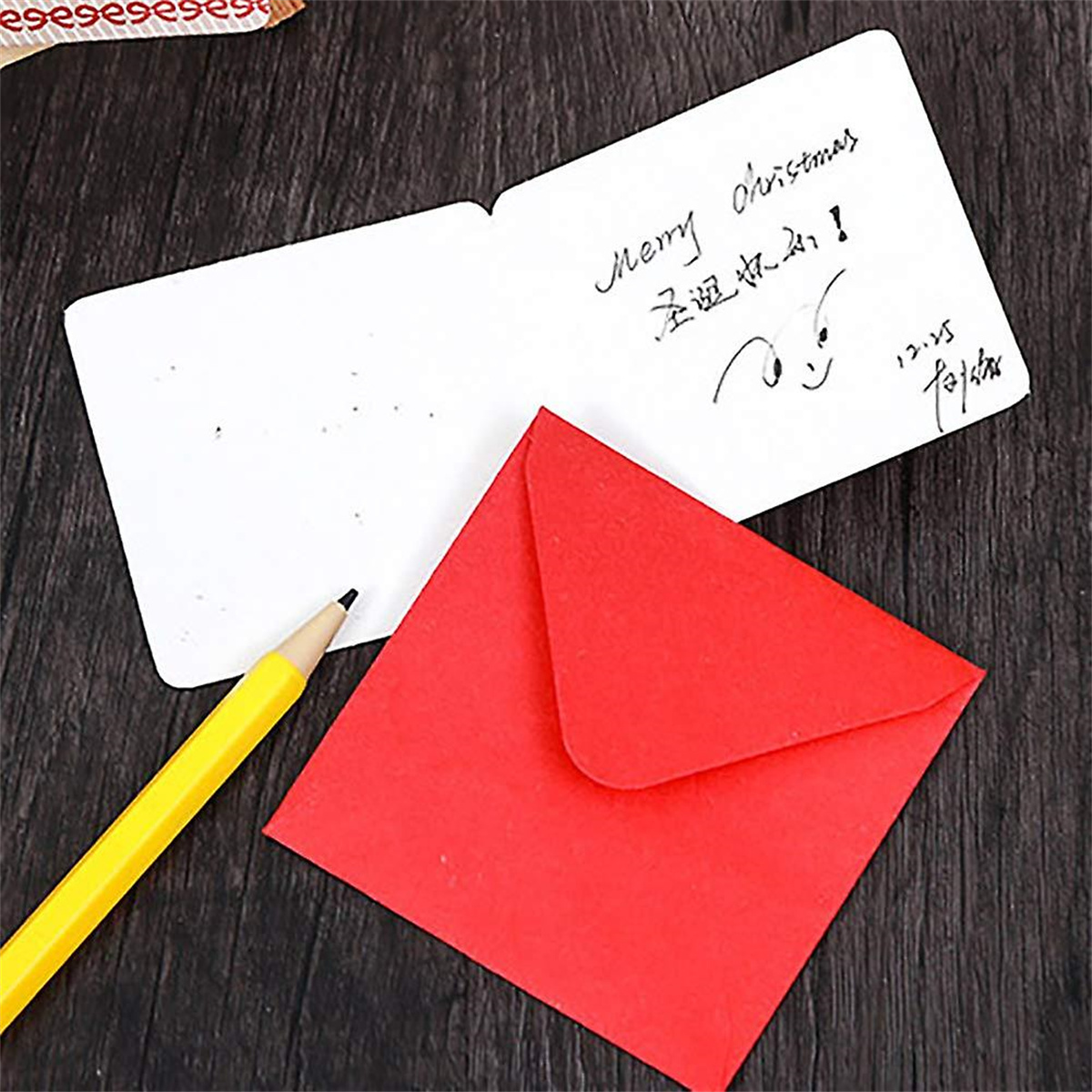 Ein gelber Bleistift neben einem roten Umschlag und einer handschriftlichen Karte mit 'Merry Christmas'.