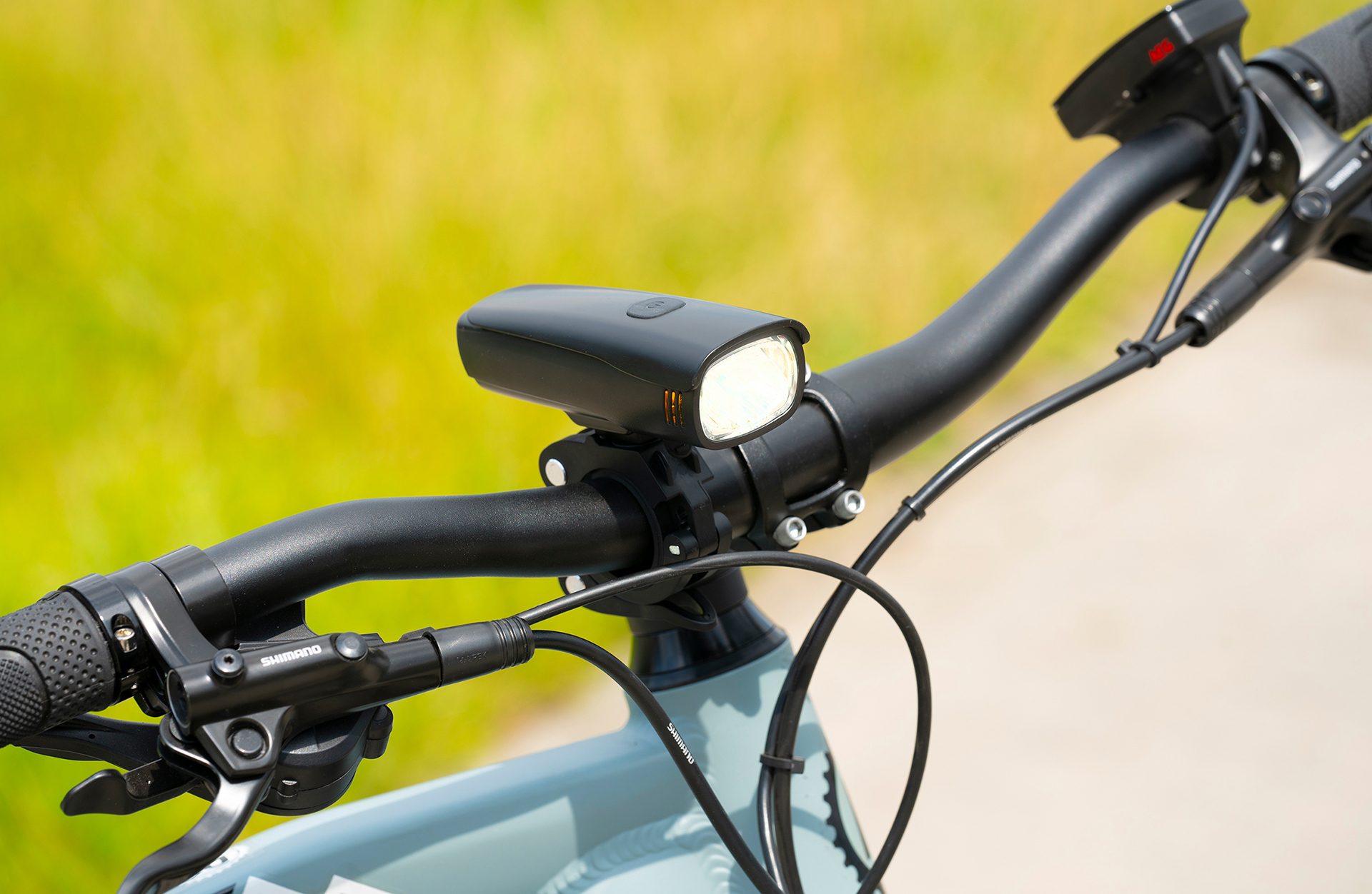 Nahaufnahme eines Fahrradlenkers mit Scheinwerfer, Bremshebel und Kabeln. Der Hintergrund ist verschwommen grün.