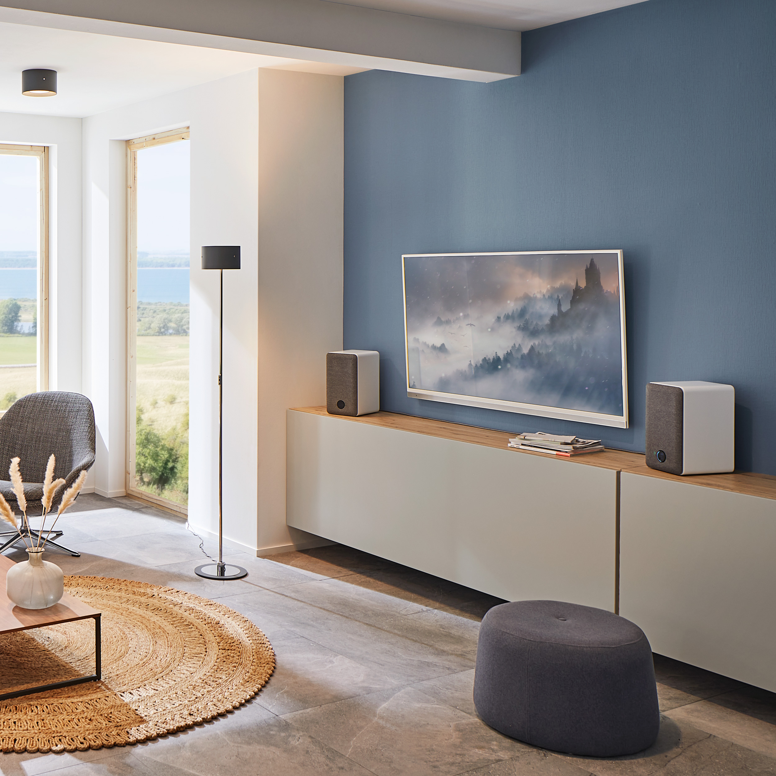 Wohnzimmer mit Fernseher, Lautsprechern, Teppich und blauer Wand.