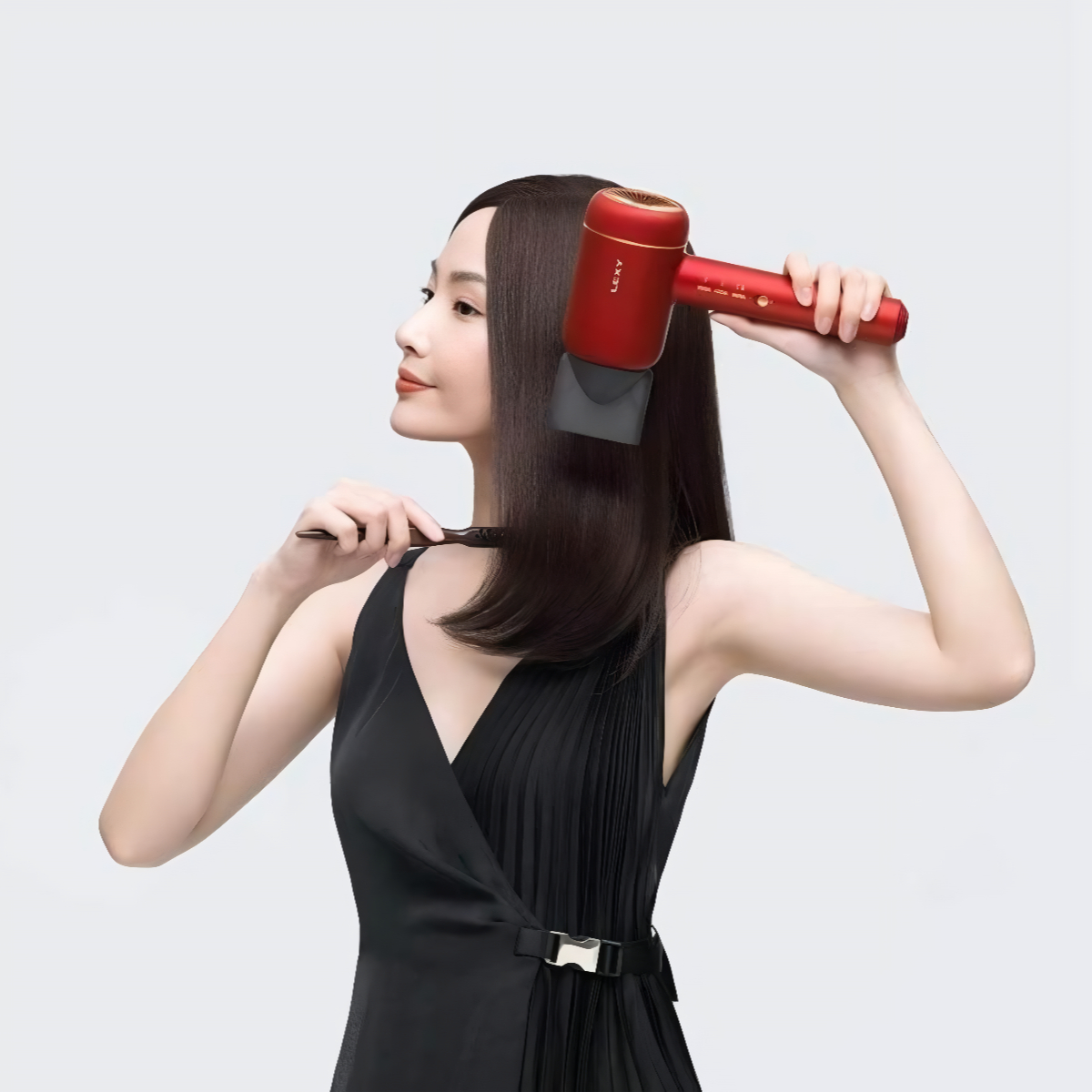 Eine Frau, die ihre Haare mit einem roten Haartrockner stylt. Sie trägt ein schwarzes Kleid.