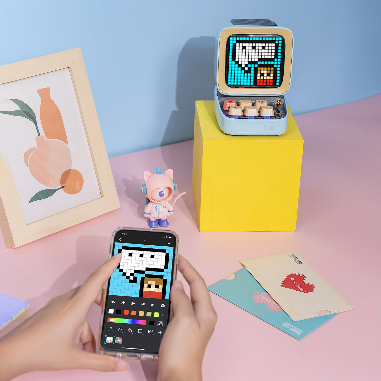 Een telefoon toont pixel art, een luidspreker, een speelgoed en een ingelijste foto staan op een roze oppervlak.