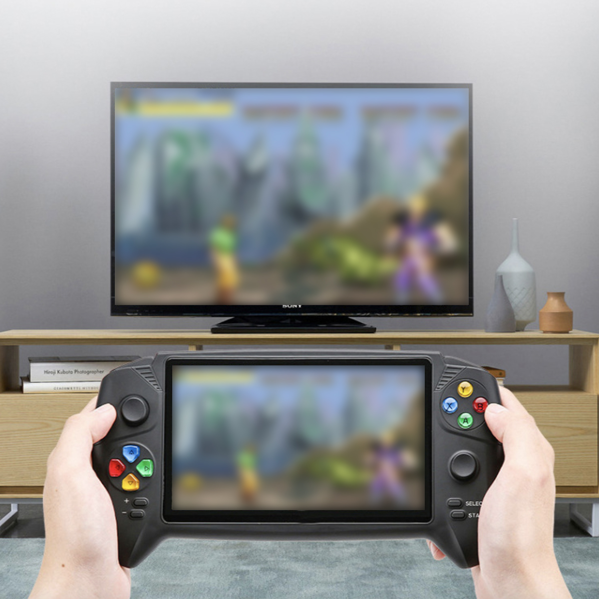 Hände halten eine Handheld-Konsole, spielen ein Spiel mit verschwommenem TV-Hintergrund.