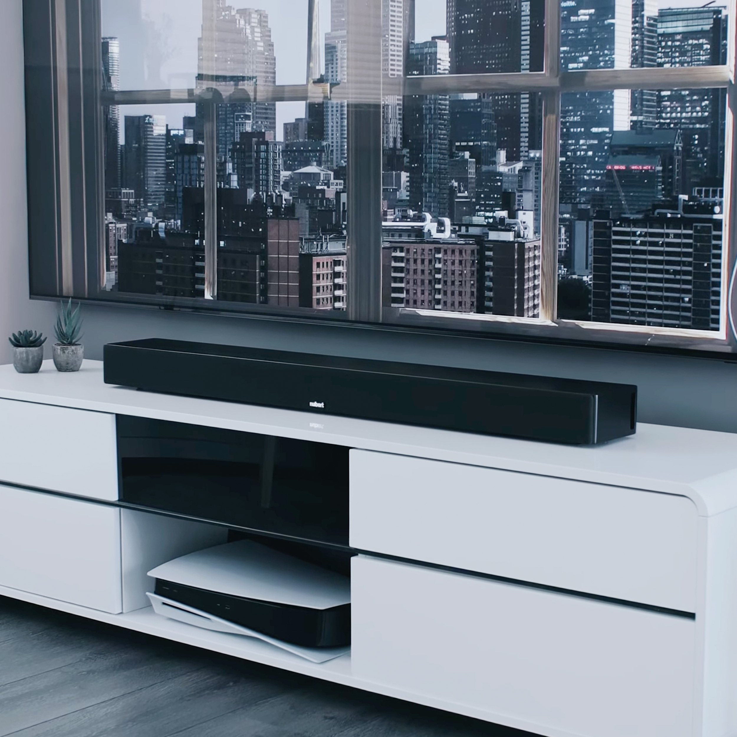 Modernes Wohnzimmer mit Soundbar auf einem weißen Schrank. Stadtbild durch das Fenster.