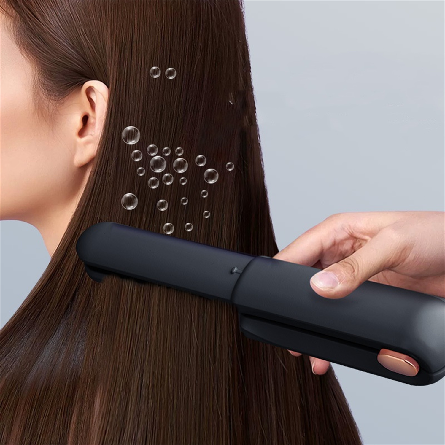 Frau benutzt eine Haarglättungsbürste. Haare sind braun. Blasen in der Luft. Grauer Hintergrund.