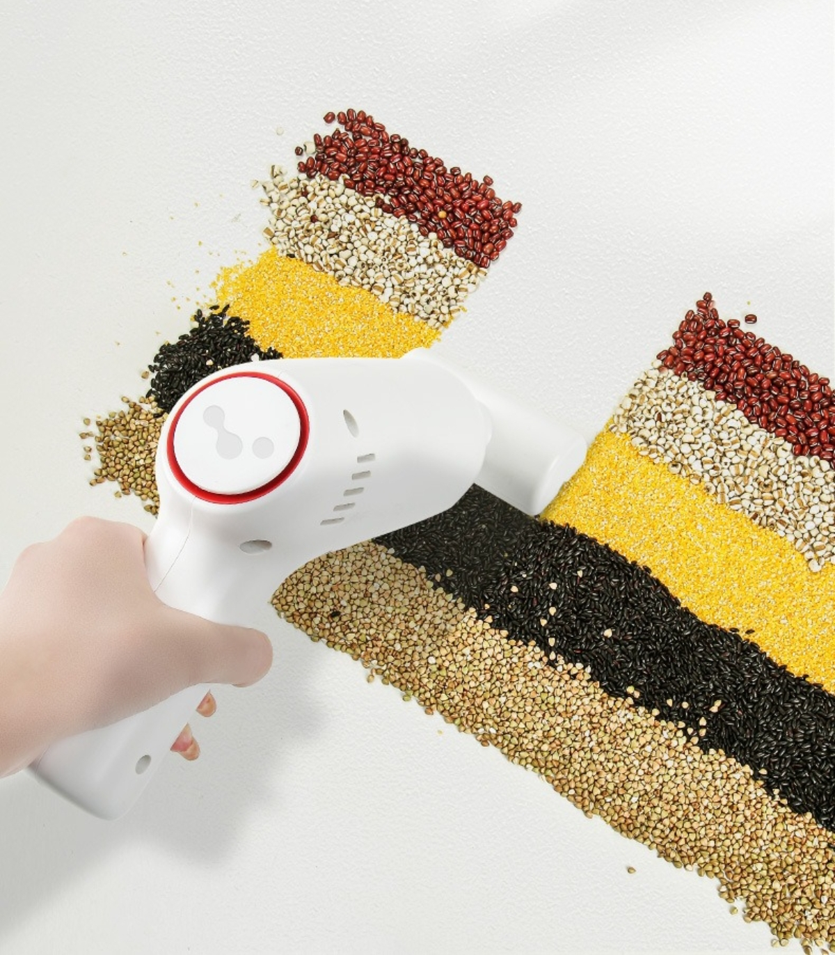 Eine Hand hält einen weißen Staubsauger über Getreide verschiedener Farben.