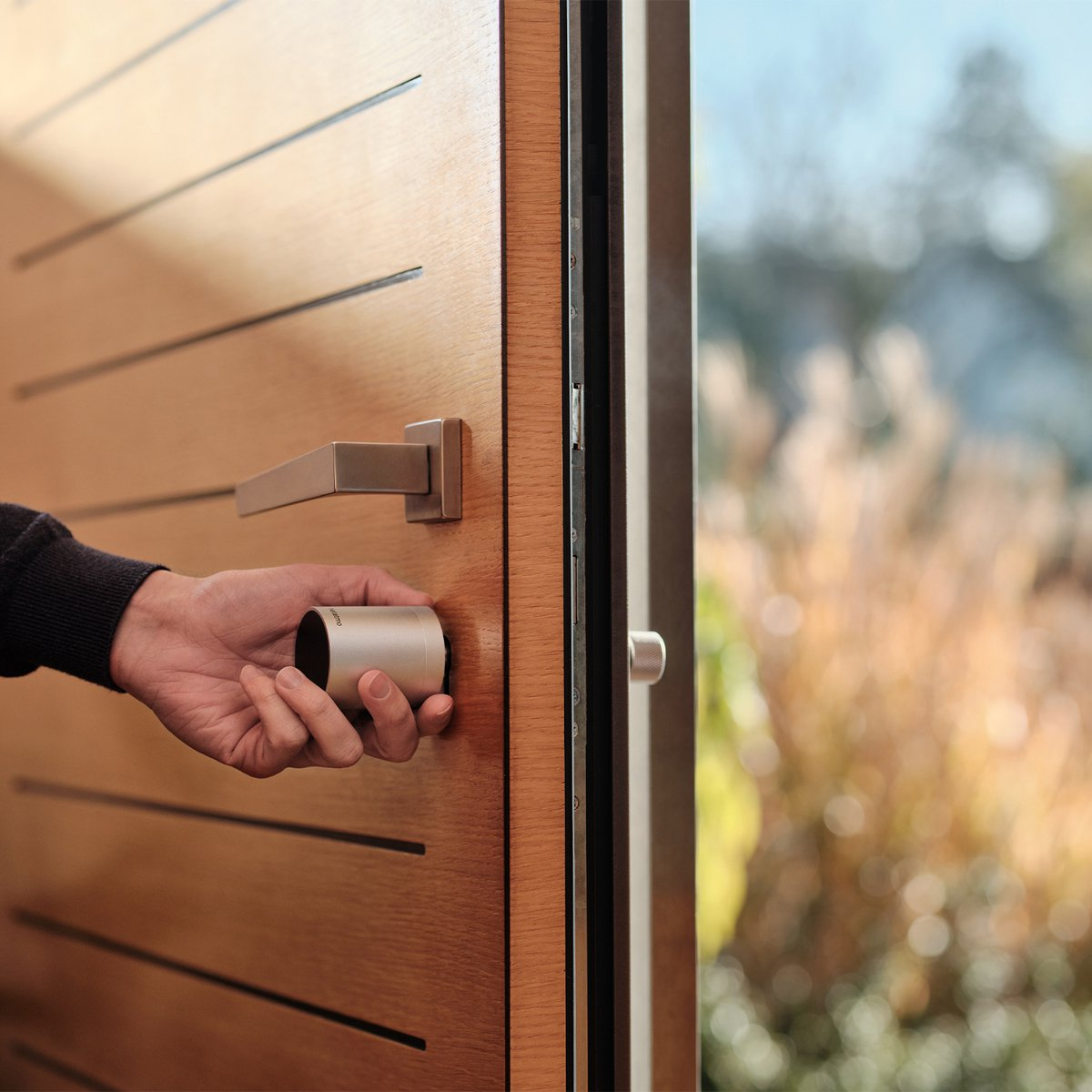 Main tenant une serrure intelligente, une porte en bois, scène extérieure floue.