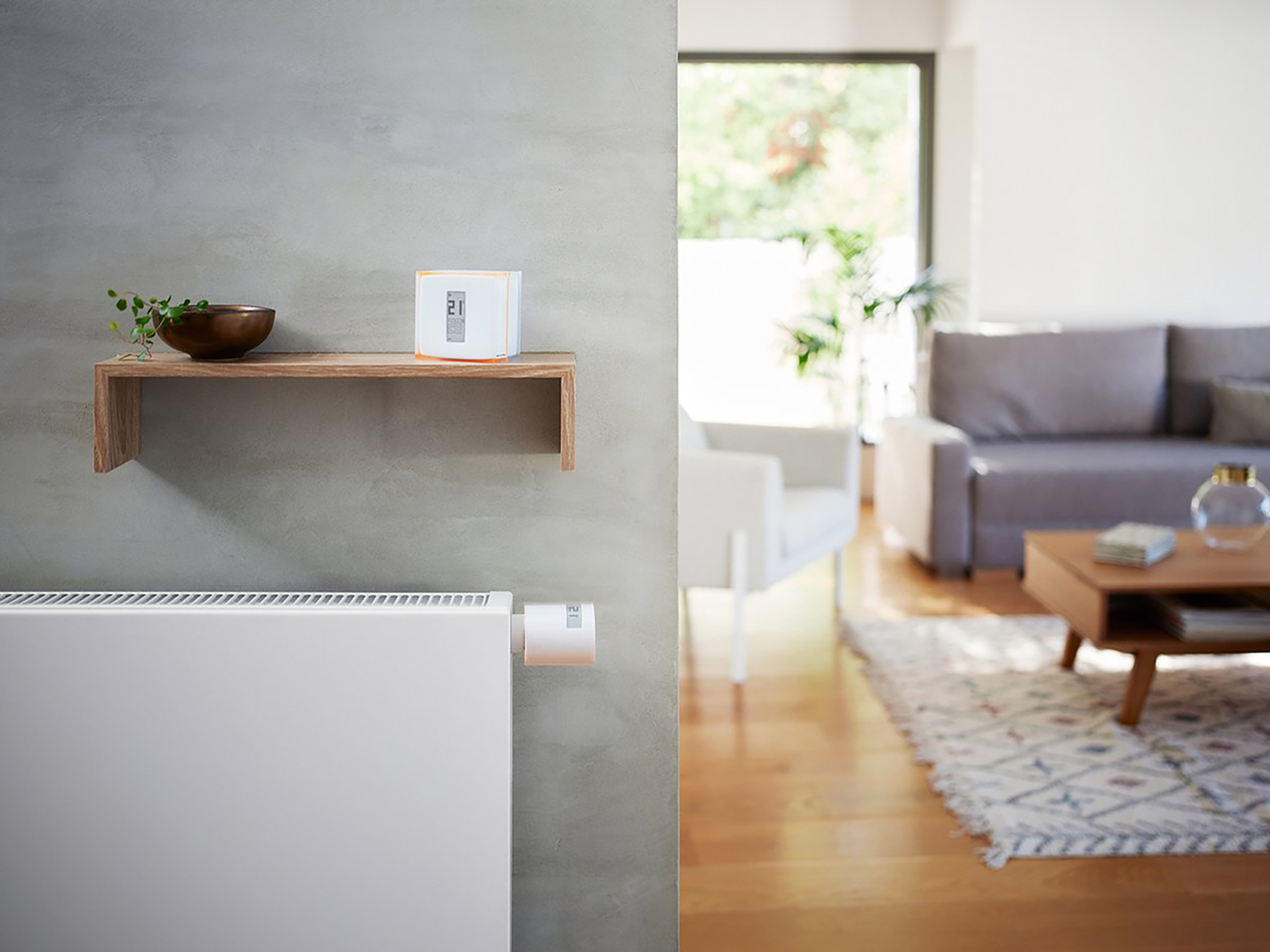 Smart home thermostat on a wall with a wooden shelf. Living room in the background.
