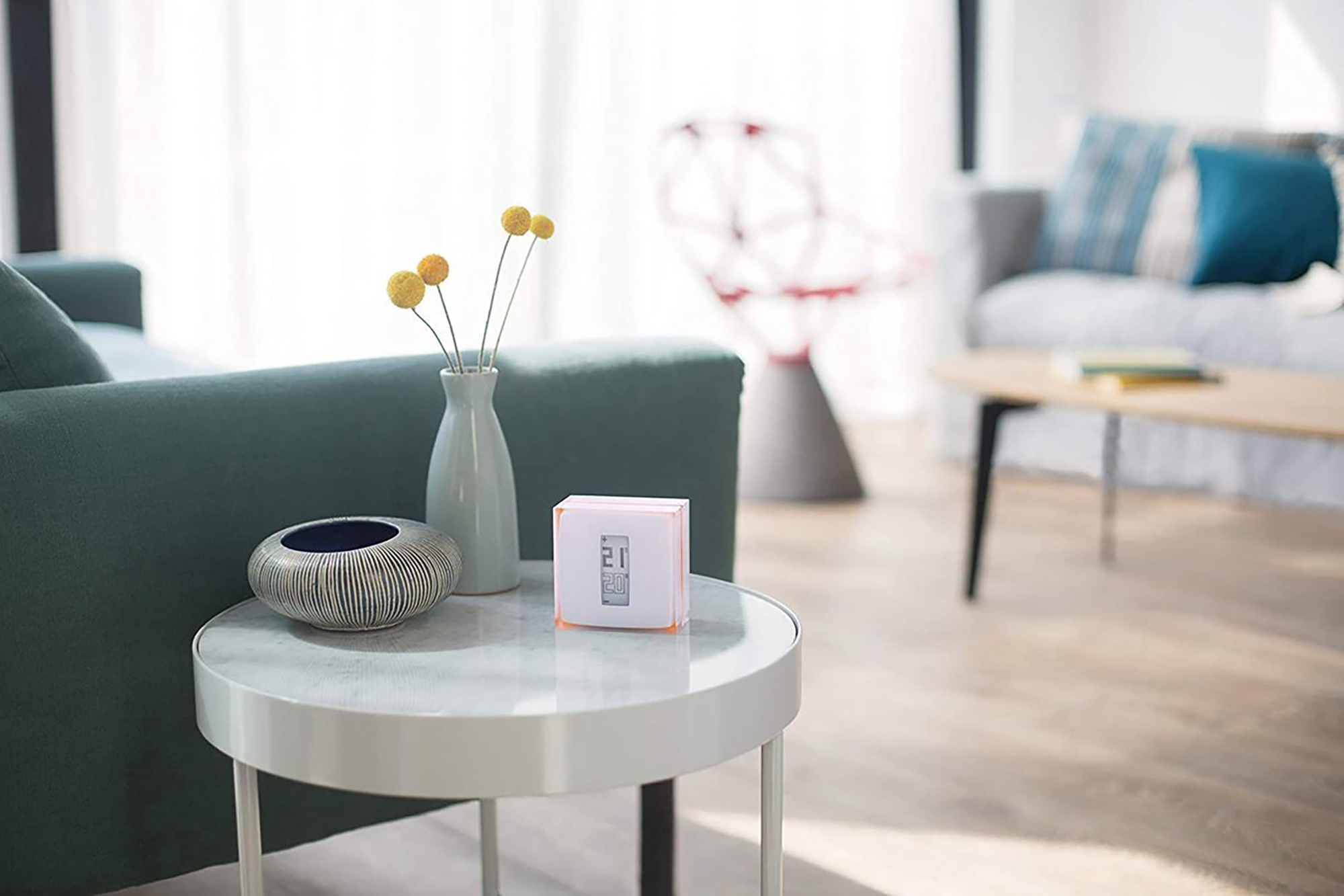 A white table with a vase and flowers, a smart cube, and a sofa in the background.