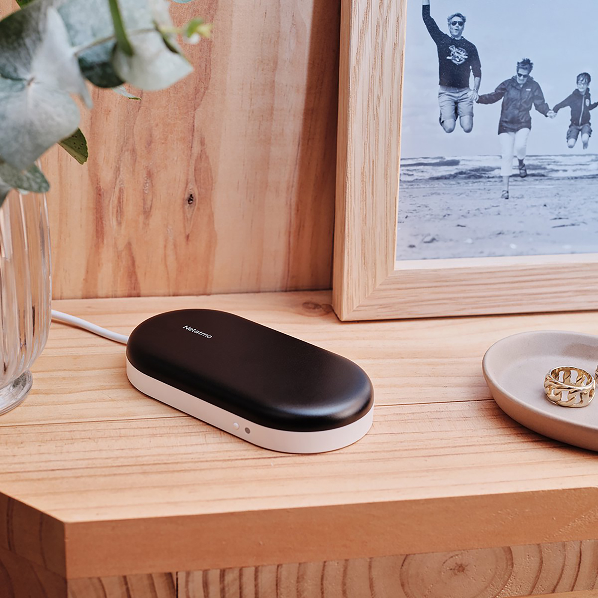 Black Netatmo device on wooden surface, with family photo and decor.