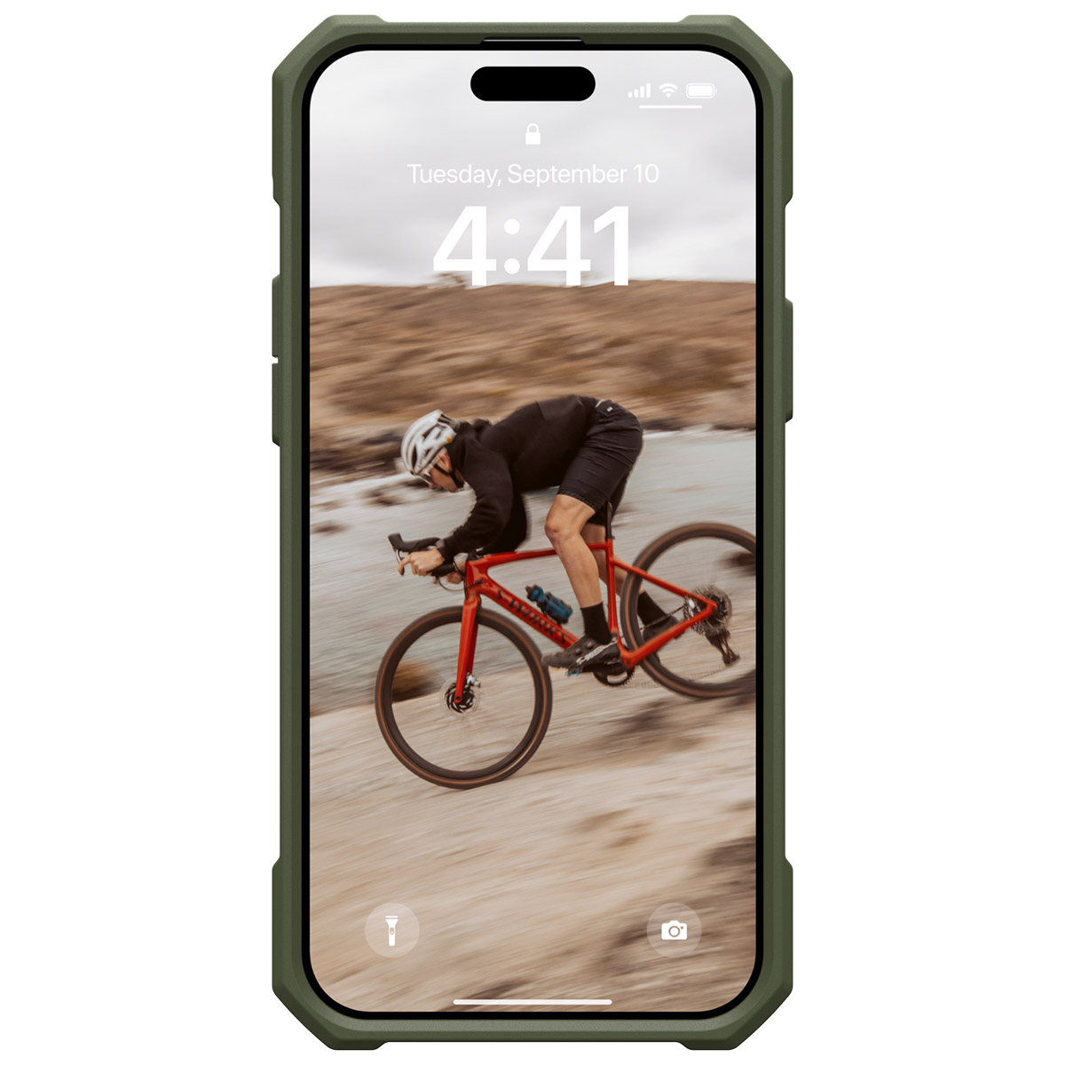 A cyclist on a red bike rides on a rocky path. The phone displays the date and time.