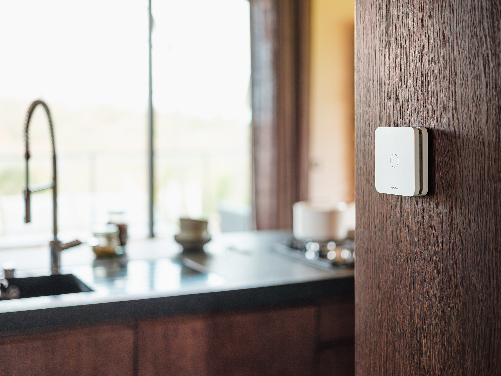 Weißer Smart Switch an einer Holzwand in einer Küche. Küchenarmatur im Hintergrund.