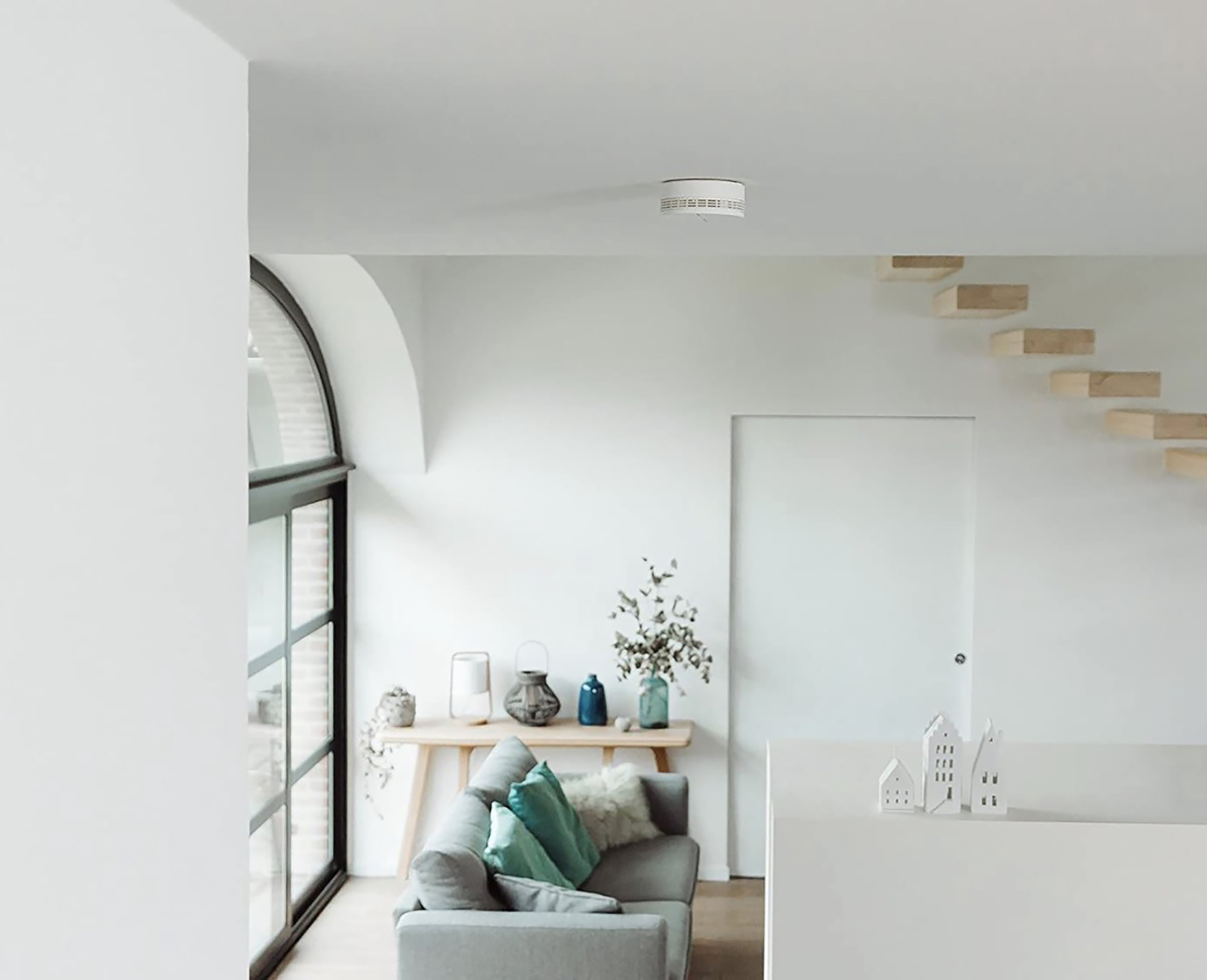 Living room with white walls and a smoke detector. A couch, table, and plants are visible.