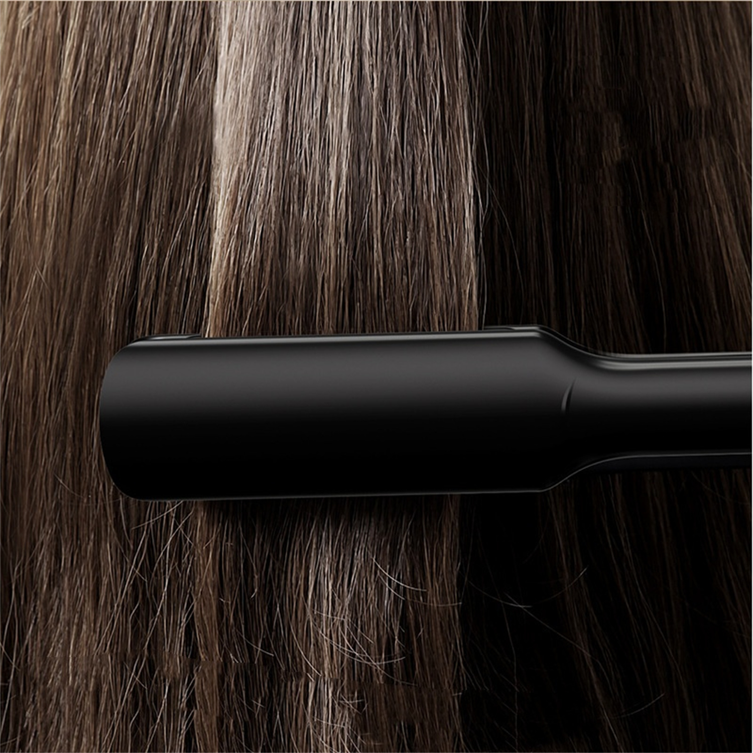 Haare, die mit einem schwarzen Glätteisen gestylt werden. Das Haar ist braun mit helleren Strähnen.