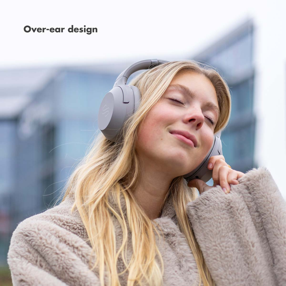 Eine blonde Frau mit grauen Kopfhörern, geschlossenen Augen, lächelnd. Der Text lautet: Over-ear-Design.