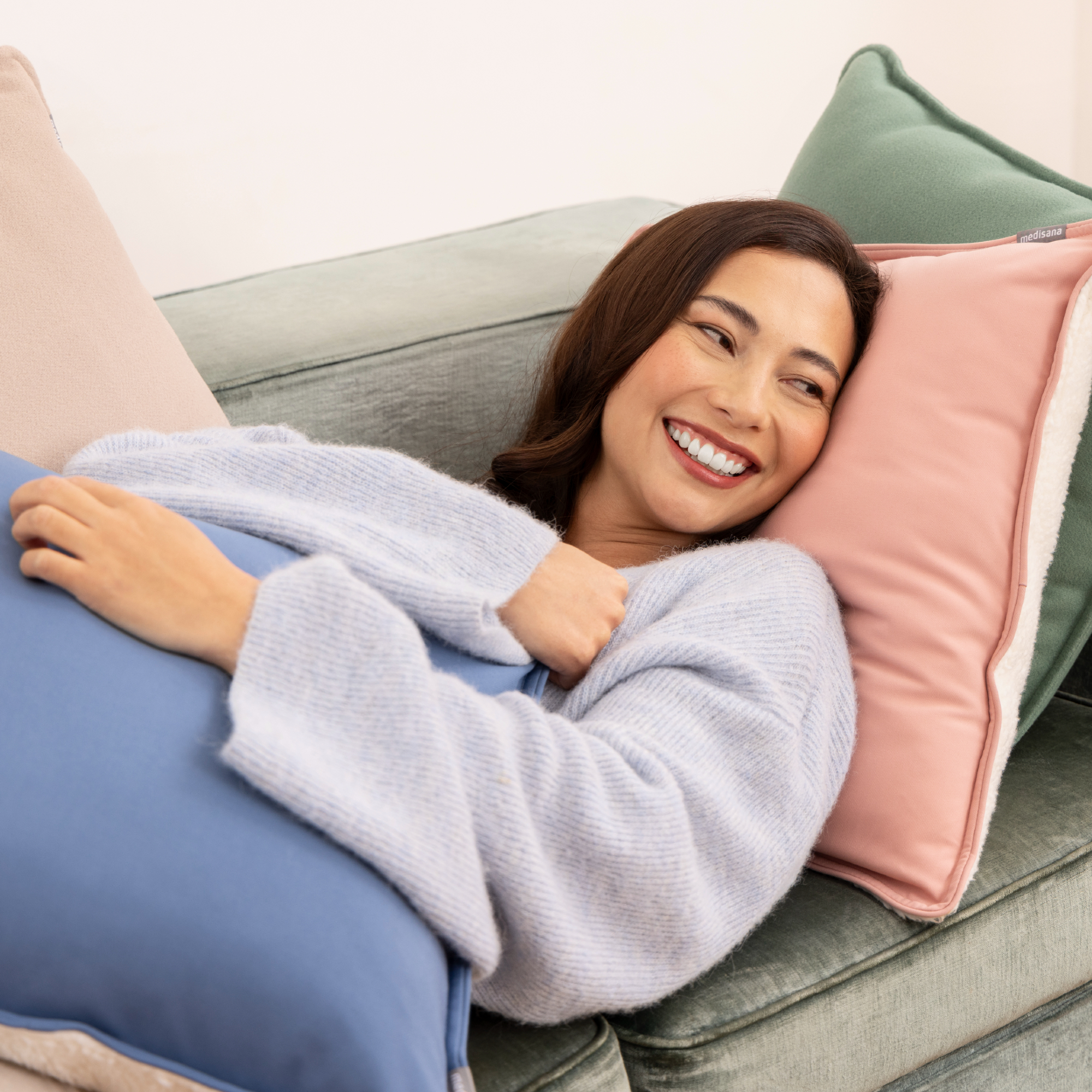 Una mujer sonriendo y acostada en un sofá con almohadas, en colores azul claro y rosa.