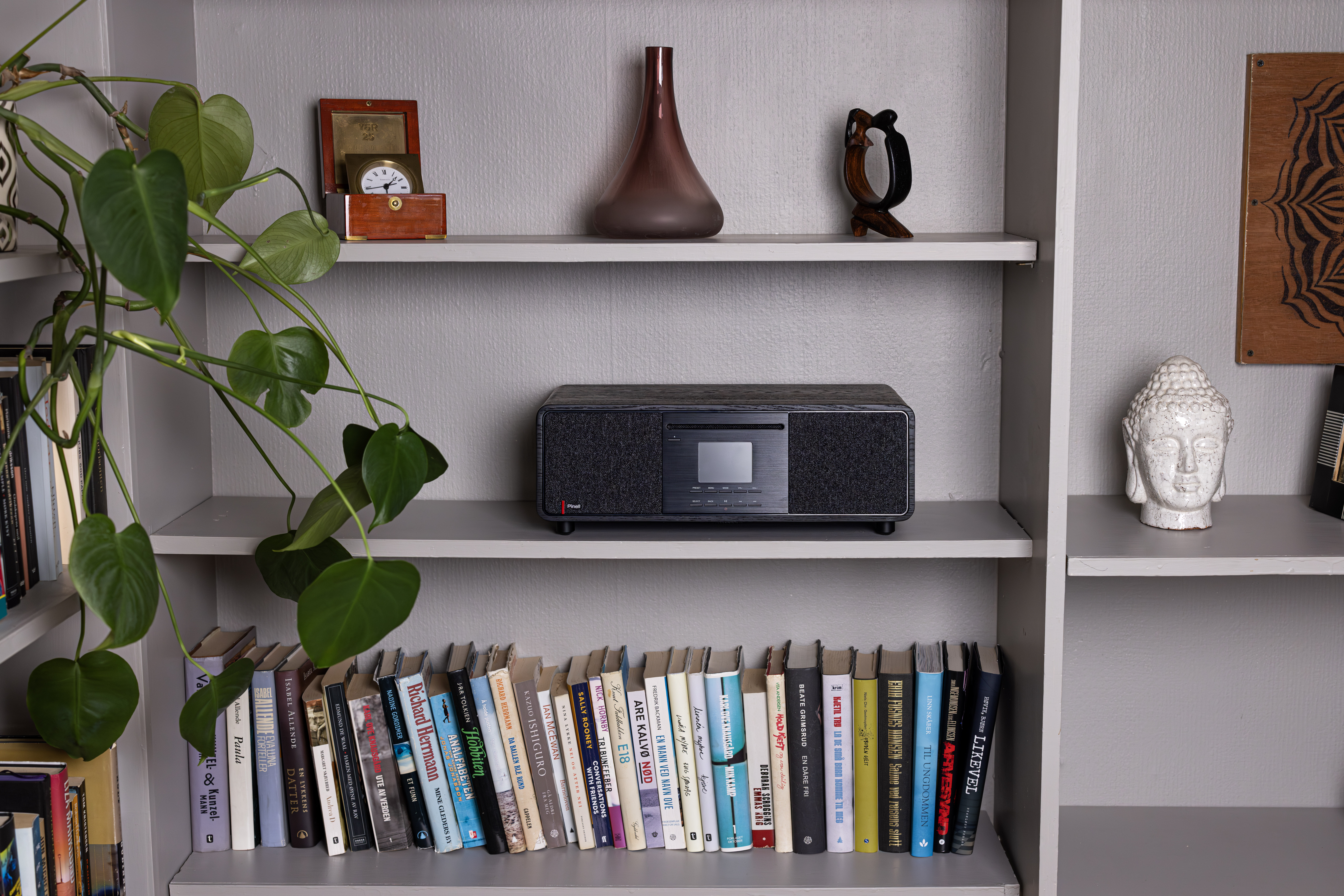 Bookshelf with books, a stereo, vase, and a plant. Shelves are grey.