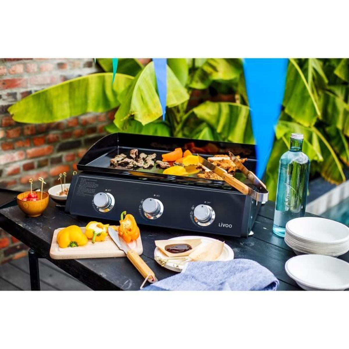 Grill mit Essen auf einem schwarzen Tisch mit verschiedenen Speisen und Wasserflasche.