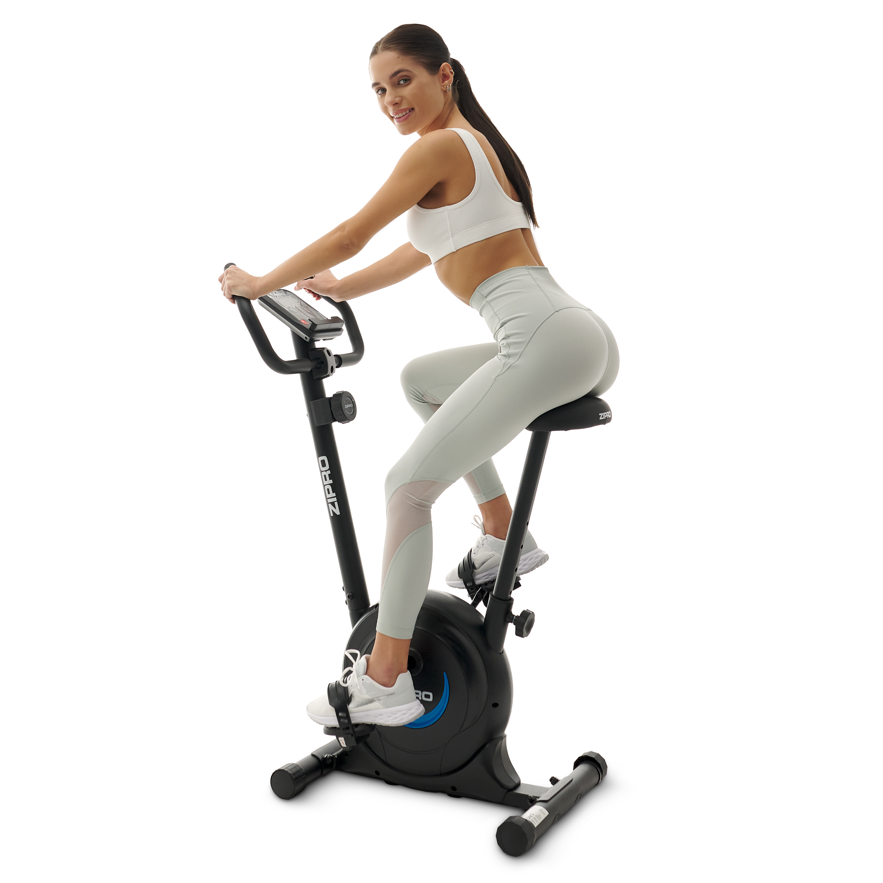 Frau auf einem stationären Trainingsfahrrad, trägt Sportkleidung. Sie lächelt und schaut in die Kamera.