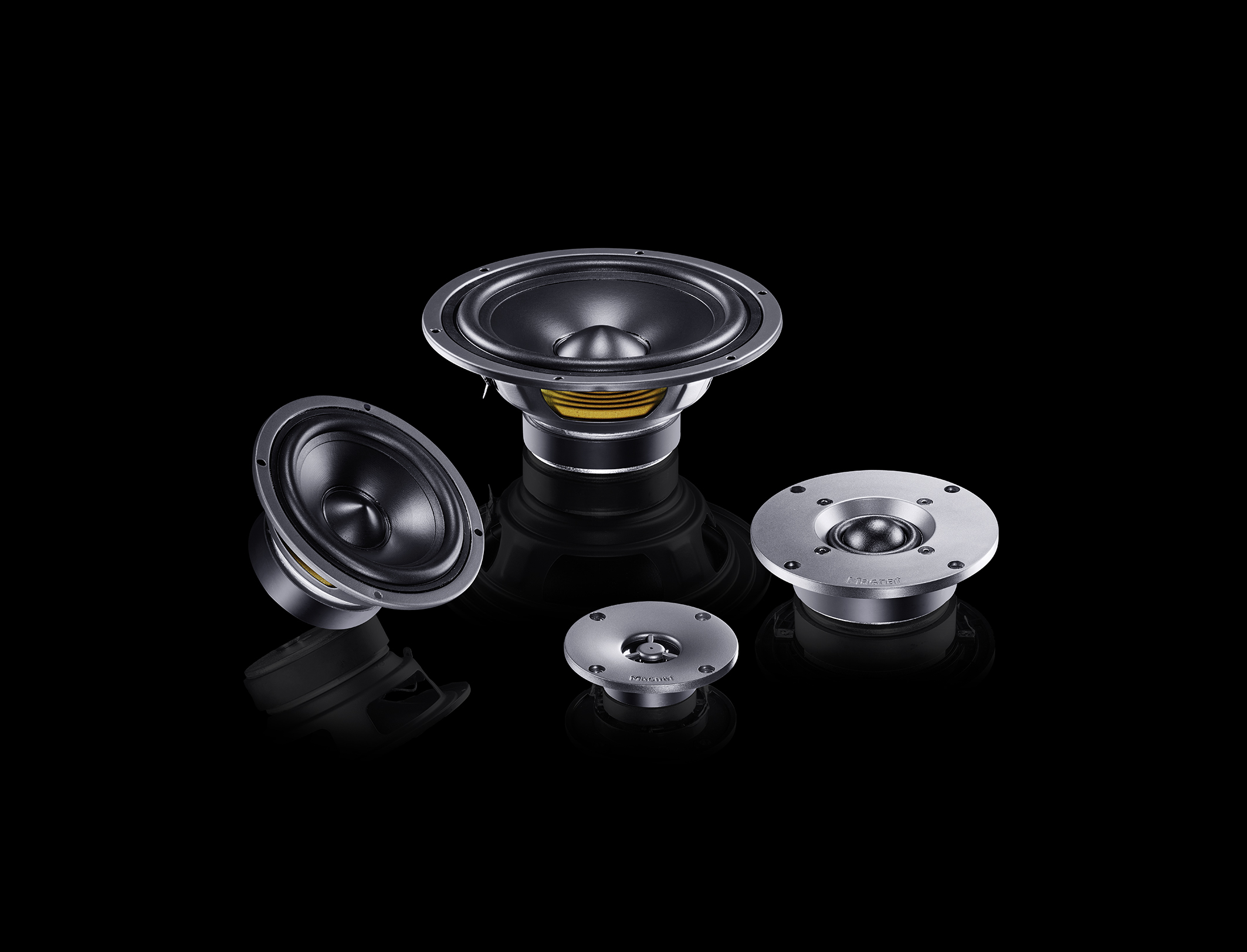 Cztery czarne elementy głośników ułożone na czarnej, odblaskowej powierzchni.