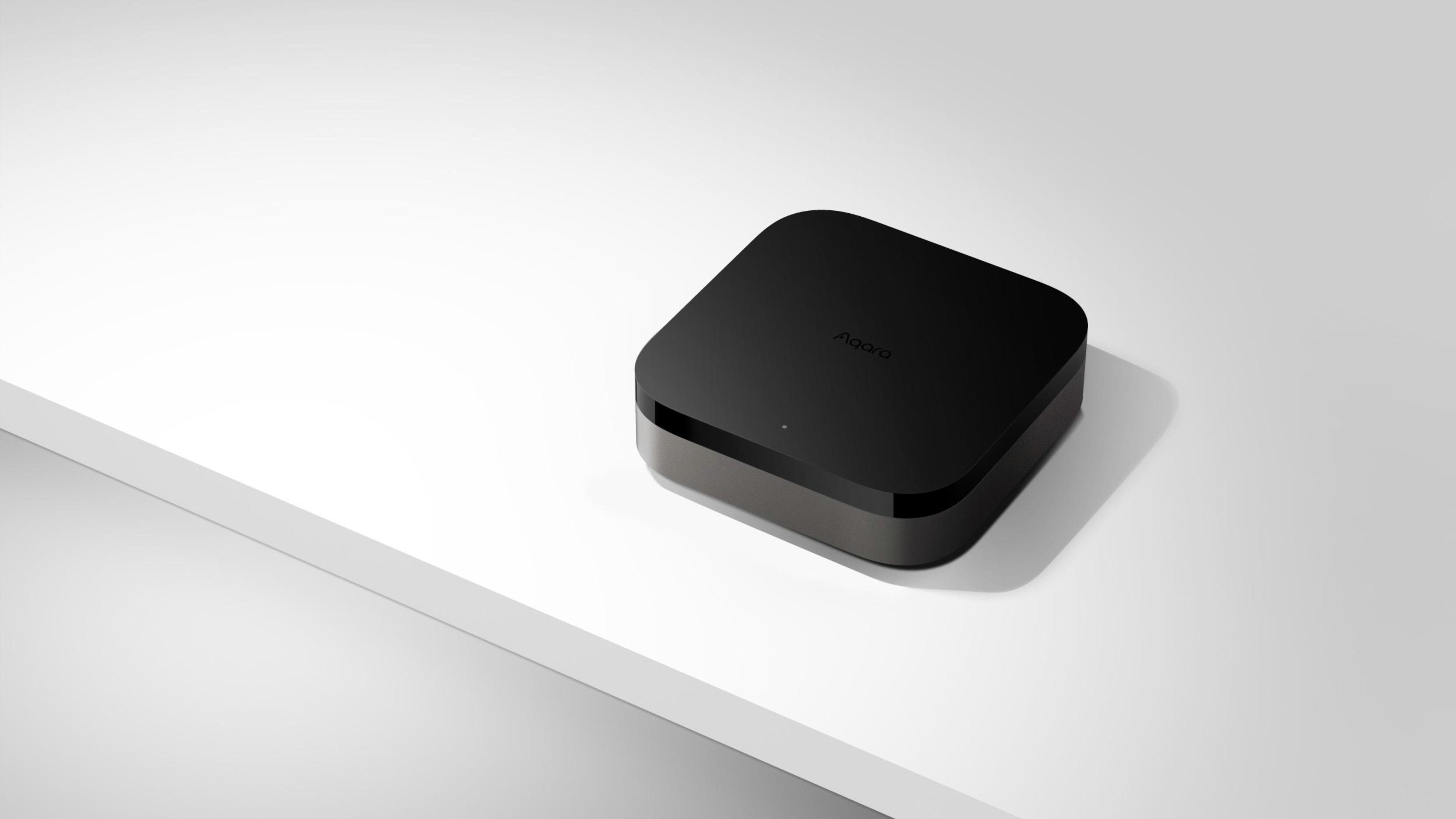 Ein schwarzer Aqara Smart Home Hub auf einer weißen Oberfläche. Die Oberseite ist flach, mit Aqara-Branding.
