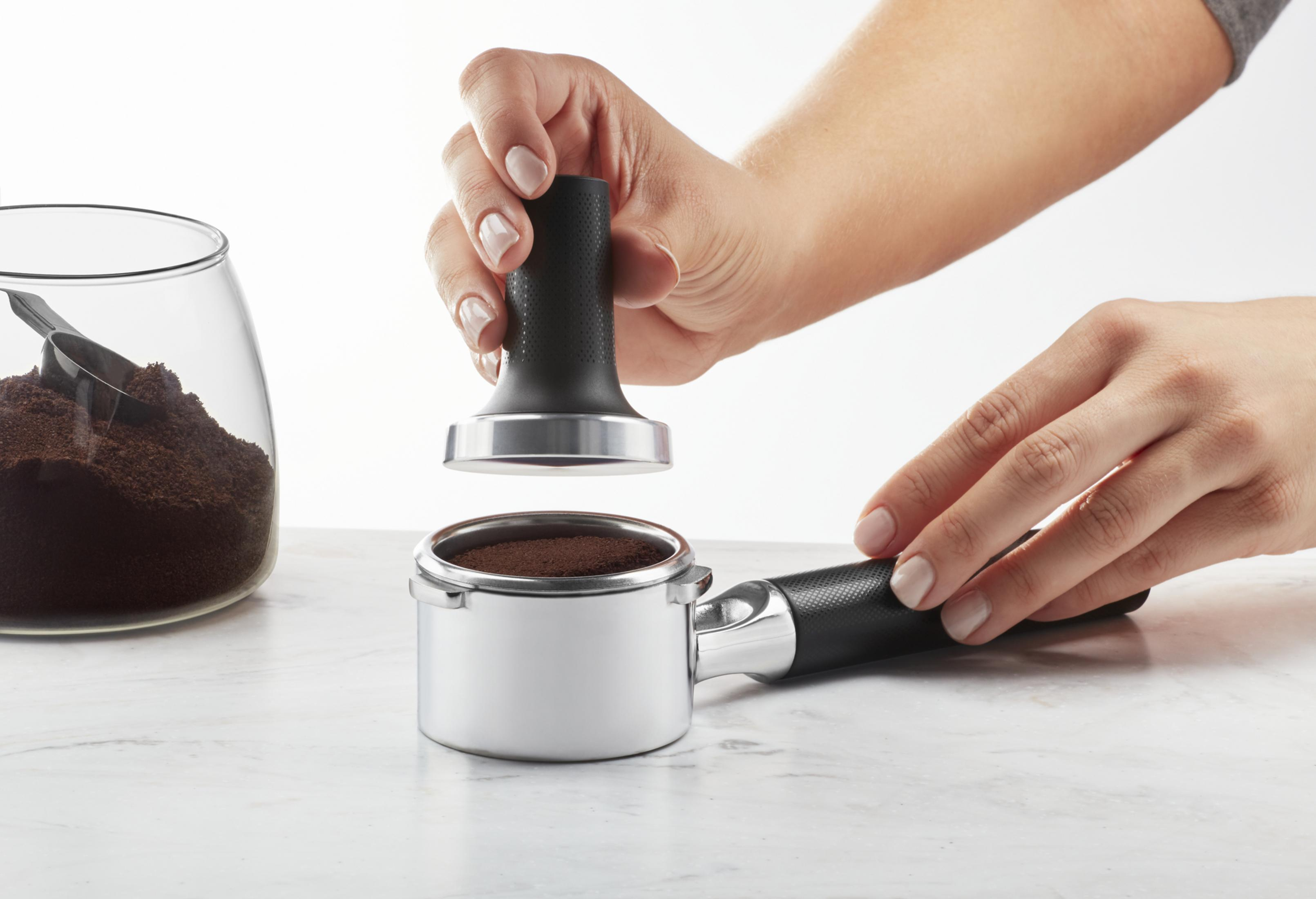 Die Hände einer Person bereiten Kaffee mit einem Tamper und einem Siebträger zu.