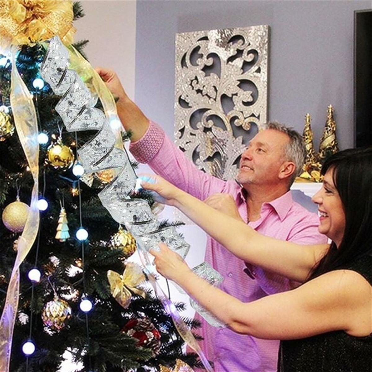 Paar schmückt einen Weihnachtsbaum mit silbernem Band und goldenen Ornamenten. Fröhliche Ausdrücke.