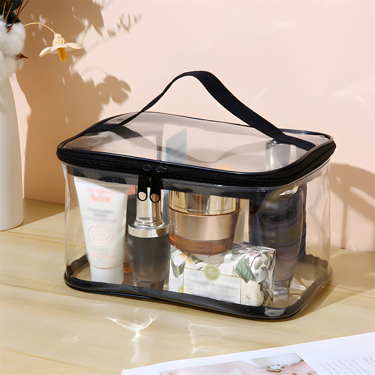 Eine transparente, rechteckige Make-up-Tasche mit schwarzem Reißverschluss und Griff. Die Tasche liegt auf einer Holzoberfläche.