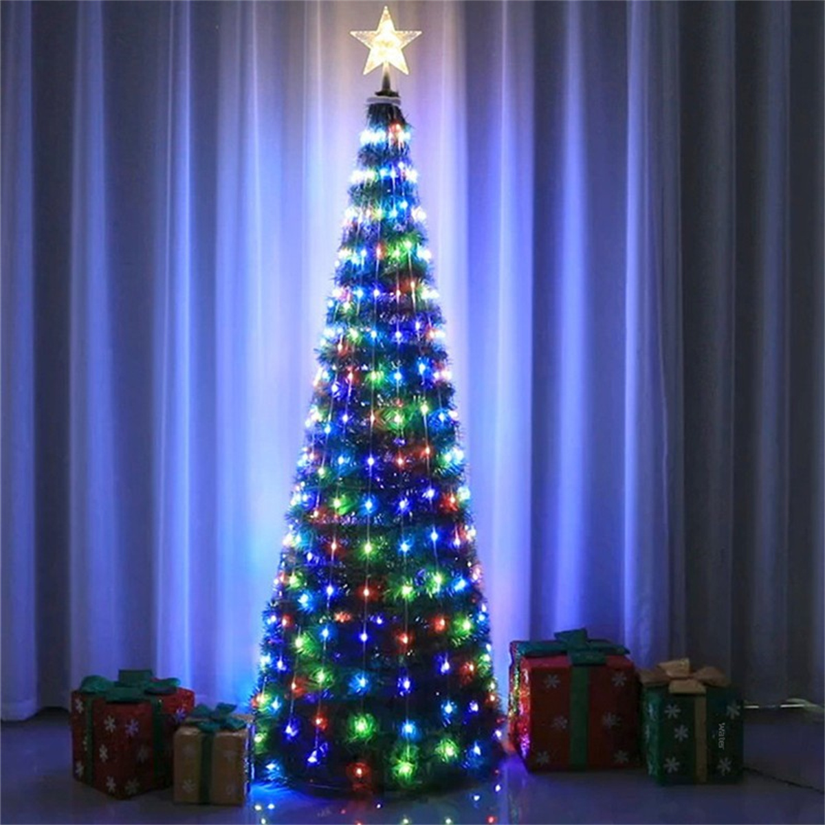 Ein beleuchteter Weihnachtsbaum mit Stern, umgeben von Geschenken. Blaue Vorhänge im Hintergrund.