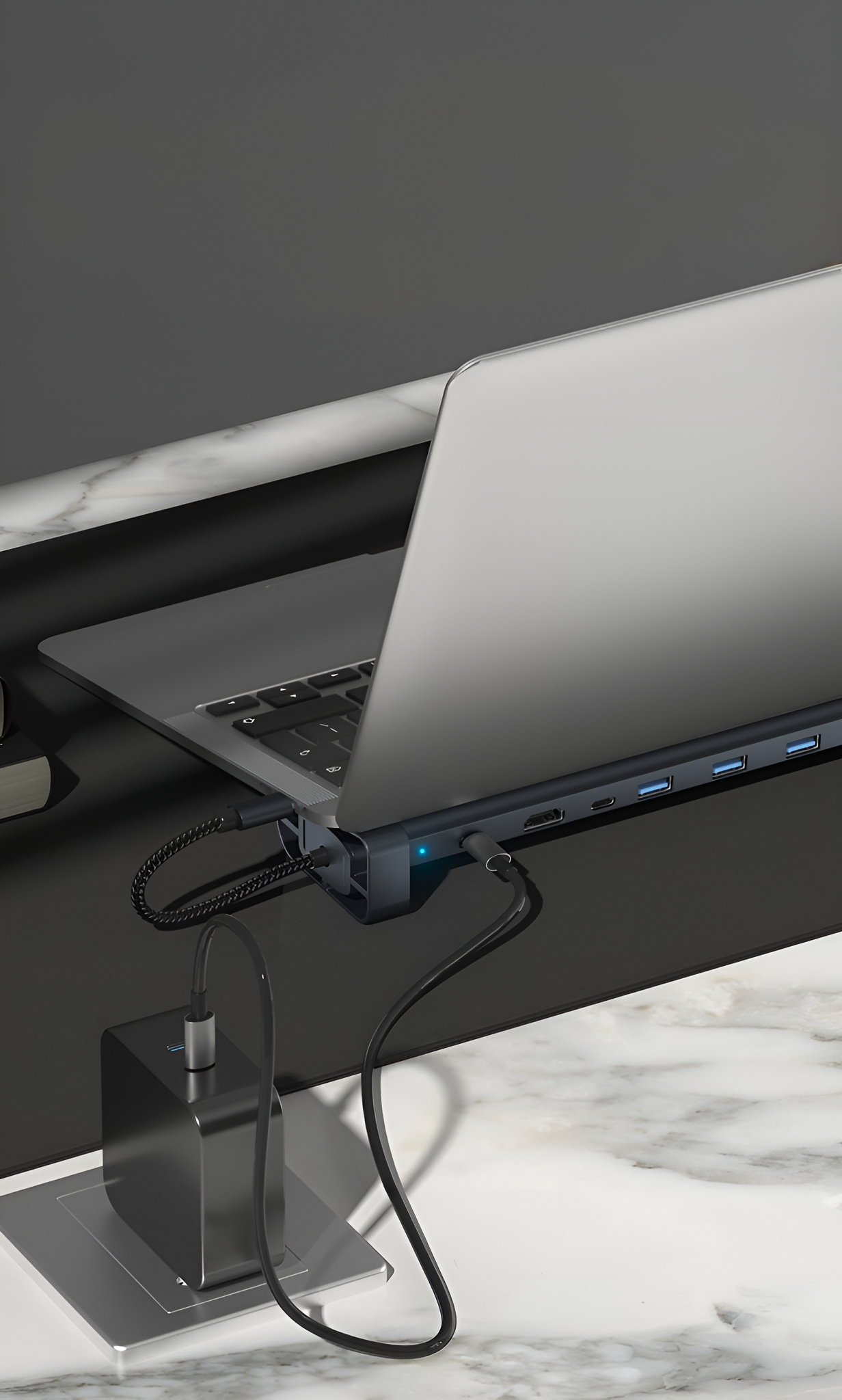 Laptop mit Hub und Kabeln, auf einem Schreibtisch neben einem Netzteil.