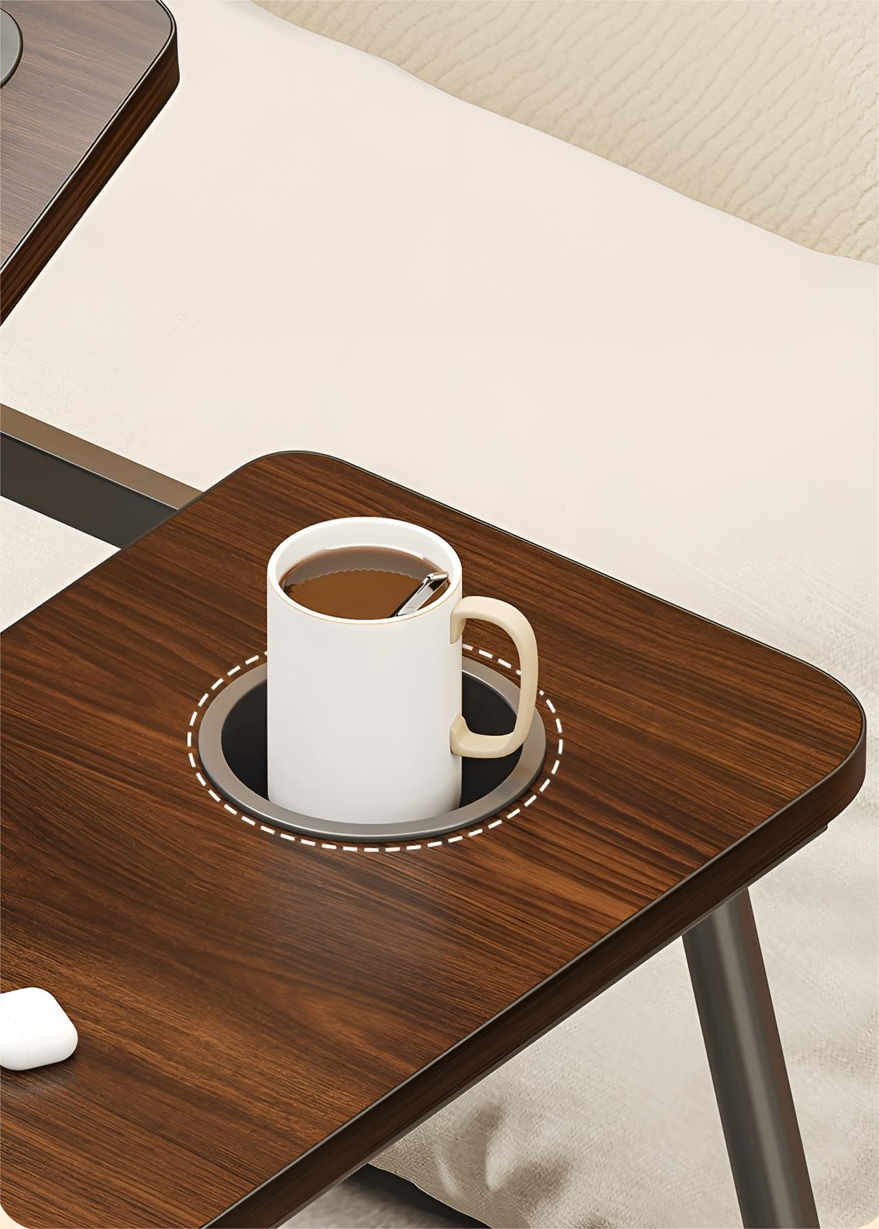 Kaffeetasse in einem Getränkehalter auf einem Holztisch. Tisch steht auf einem Bett. Cremefarbene Bettdecke.