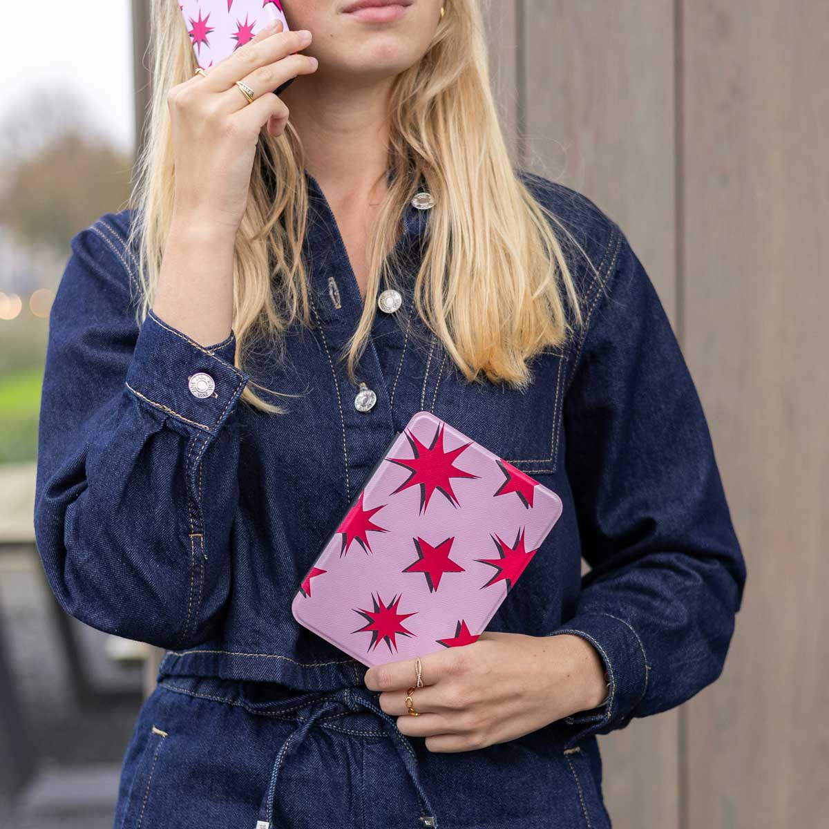 Femme en jean bleu tenant une tablette rose à motifs d'étoiles et un téléphone.