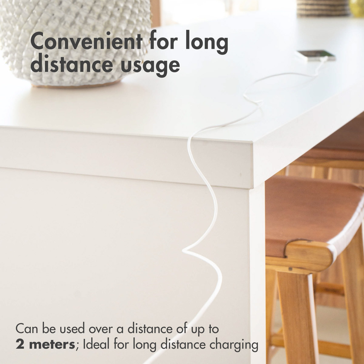 Une table blanche avec un câble blanc connecté à un téléphone. Un tabouret en bois à droite.