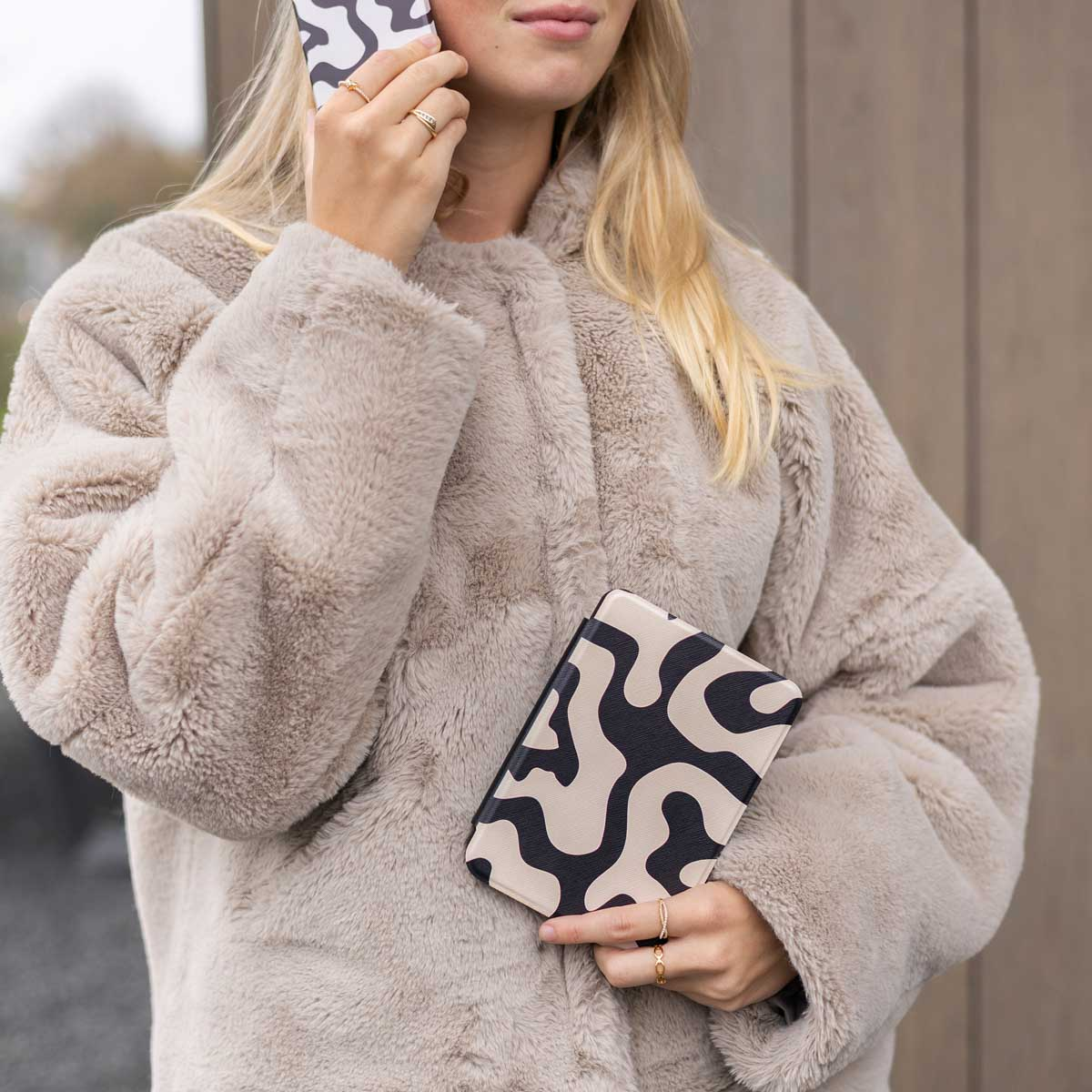 Femme en manteau de fourrure tenant un téléphone et un étui avec un motif noir et beige.